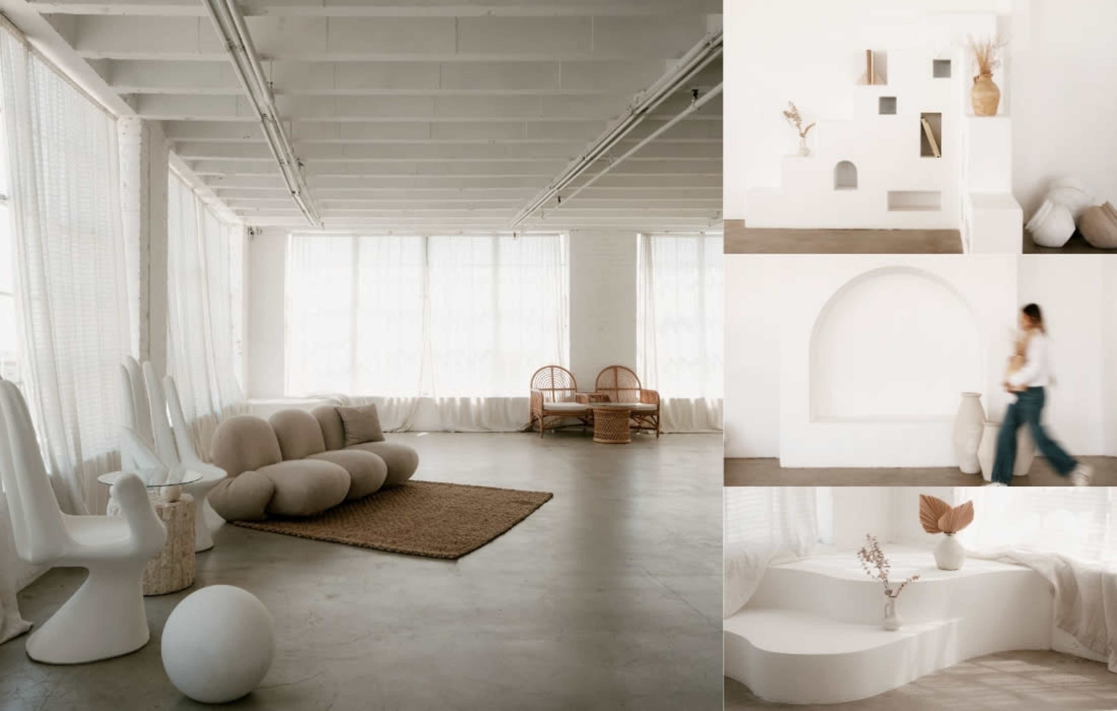 The image features a minimalist interior space with soft, neutral tones, large windows, and a mix of sculptural furniture pieces arranged around a decorative rug.