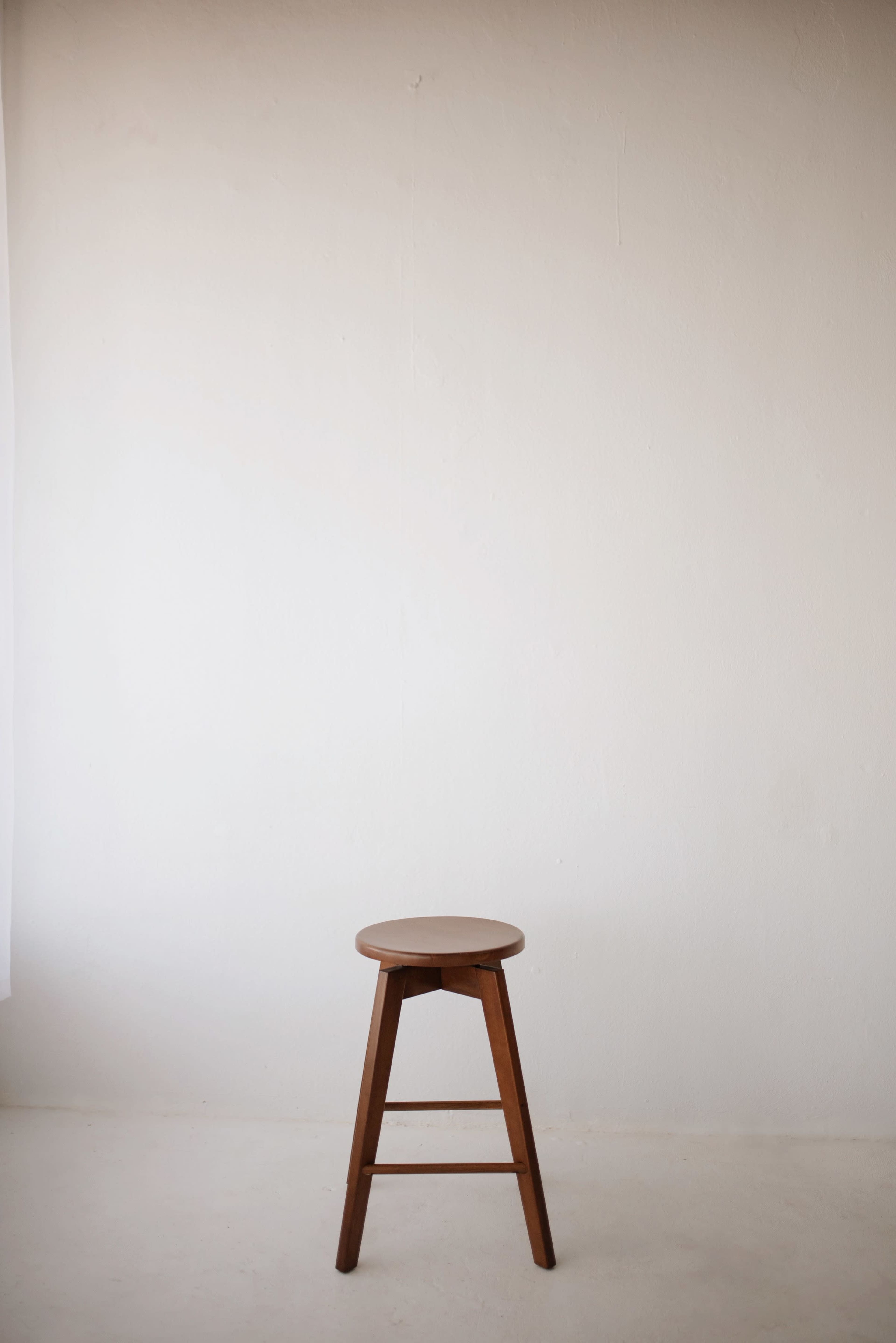 A wooden stool stands alone against a plain white wall.