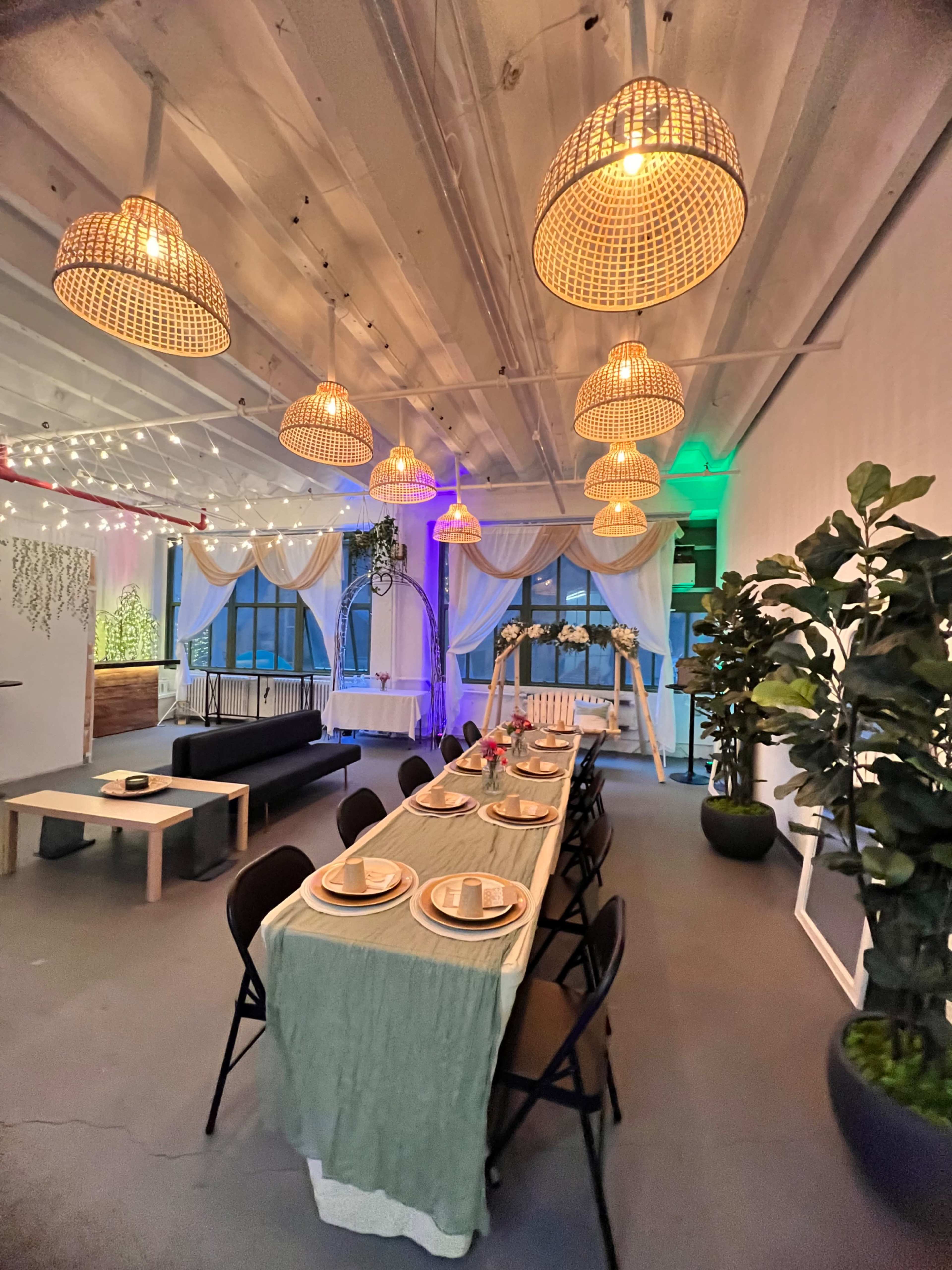 A well-decorated dining area with a long table set for a meal, surrounded by stylish pendant lights and greenery.