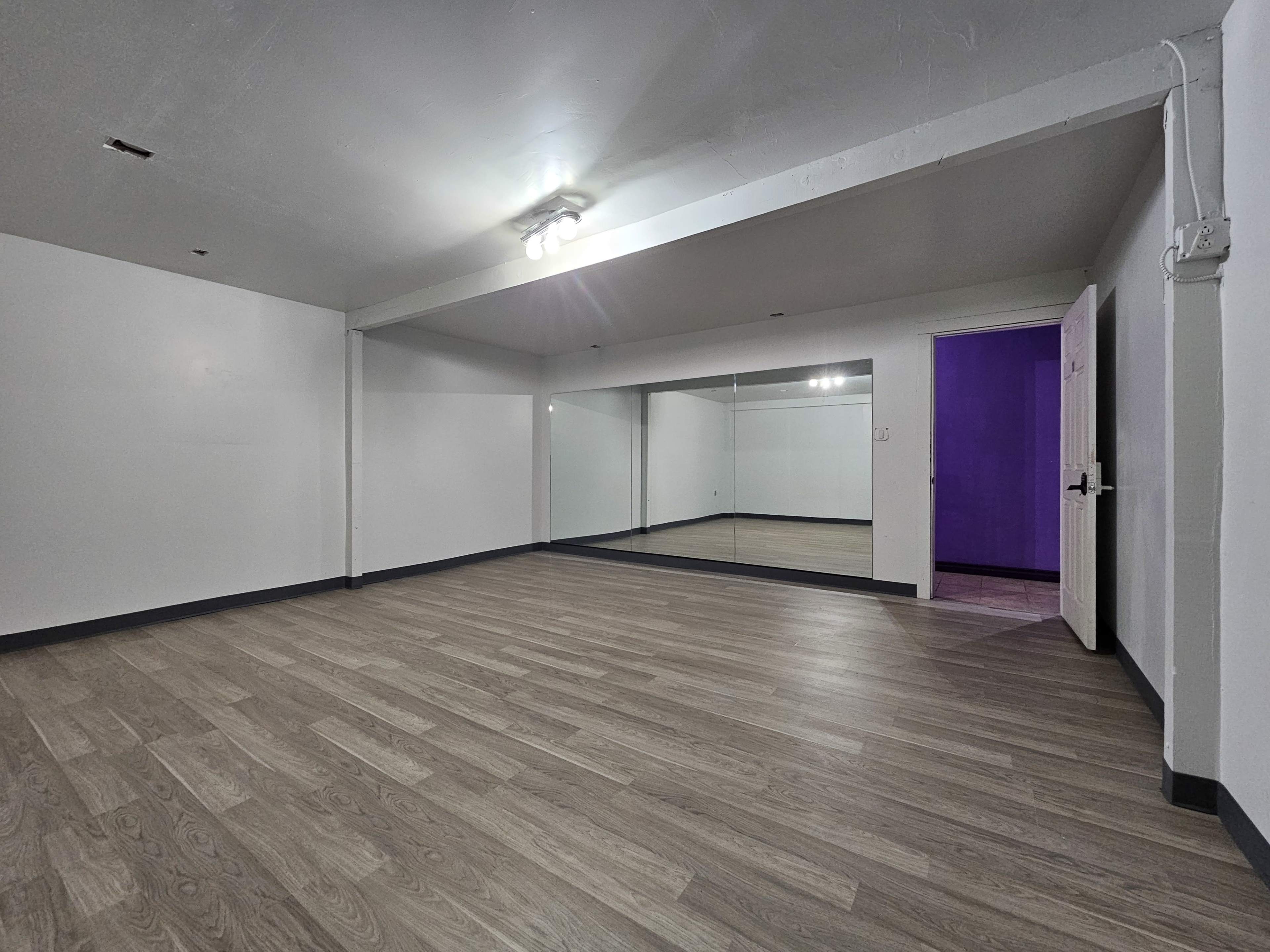 The image shows an empty room with wooden flooring, a mirrored wall on one side, and a single purple-painted door leading to another space.