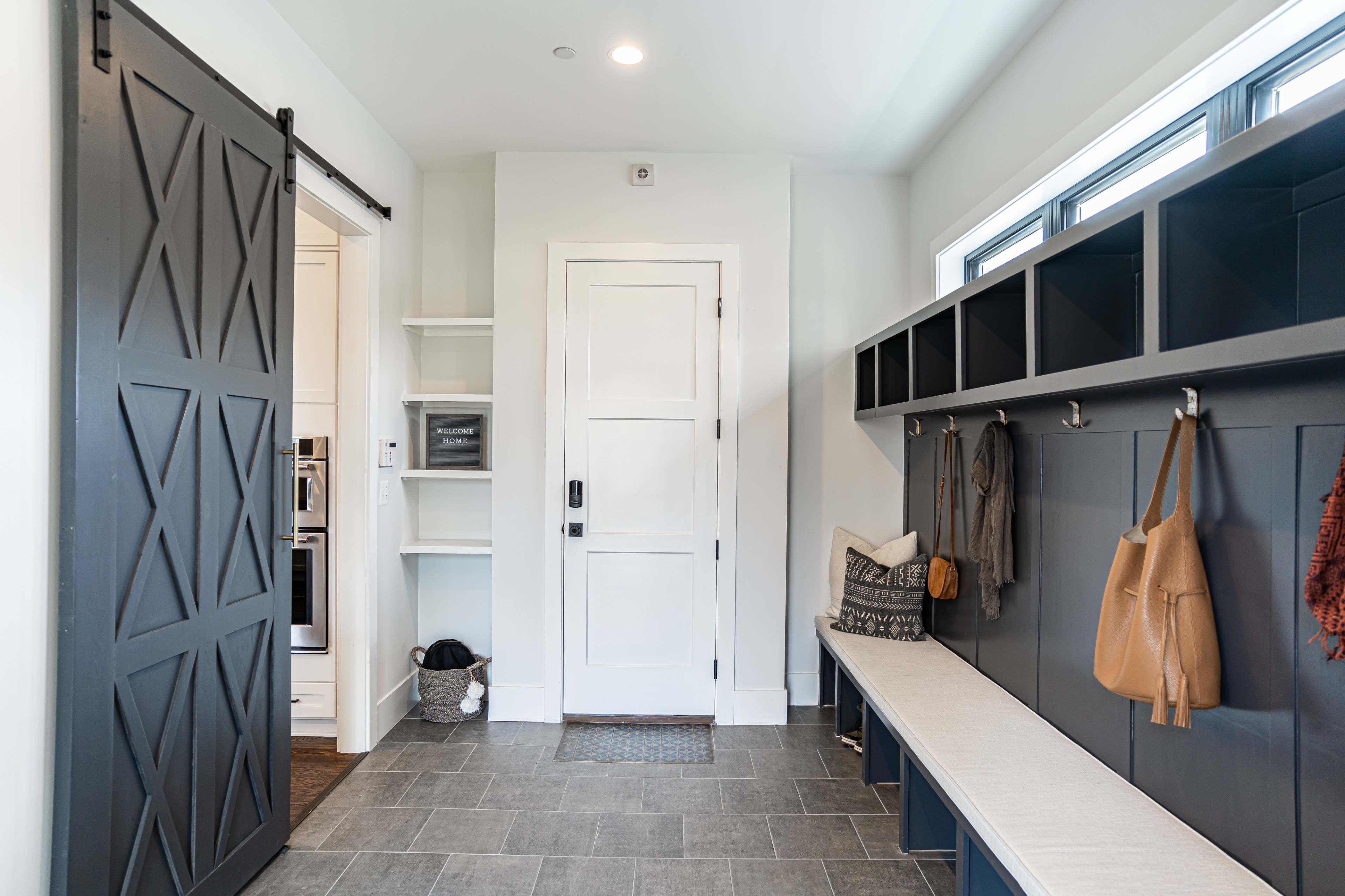 A modern entryway featuring a closet area, a bench with storage, and hooks for hanging coats and bags.