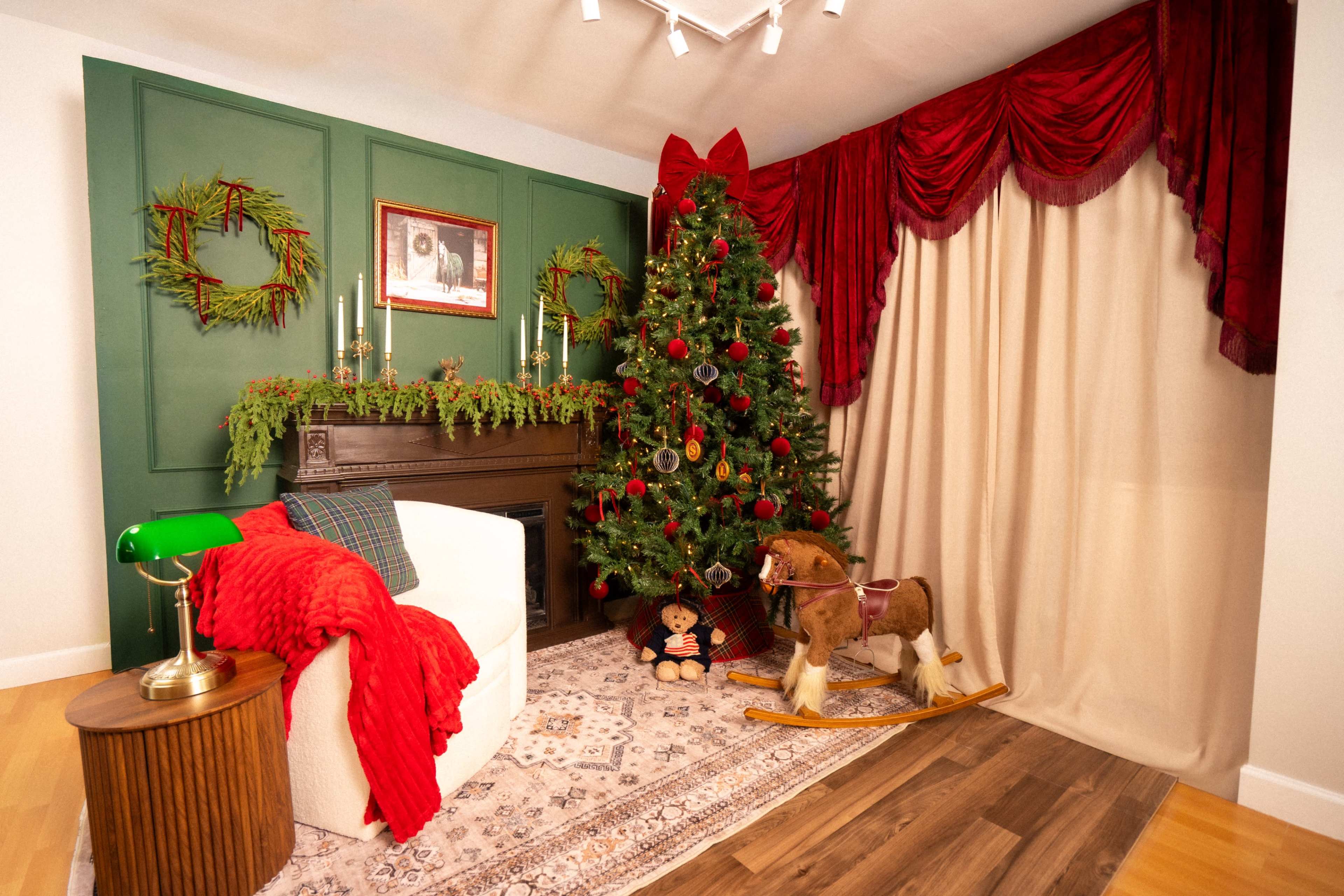 The scene features a decorated Christmas tree next to a fireplace, surrounded by festive greenery, a rocking horse, and red drapery.