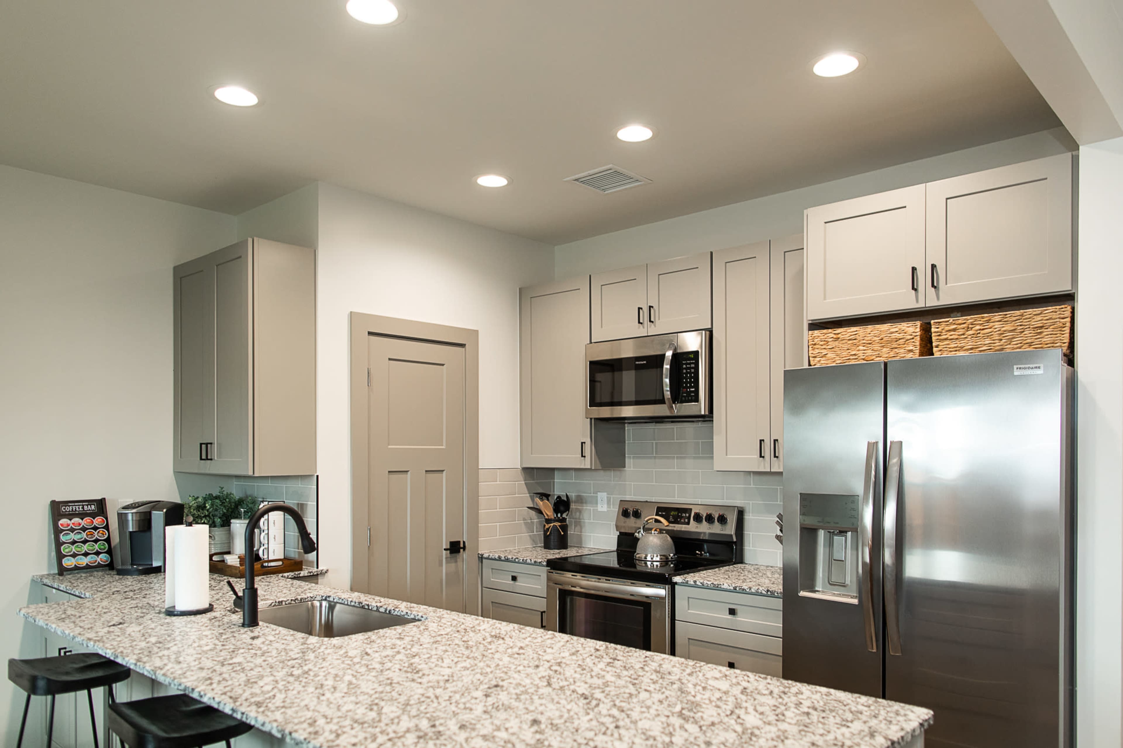 A modern kitchen featuring gray cabinetry, stainless steel appliances, and a large island with a granite countertop.