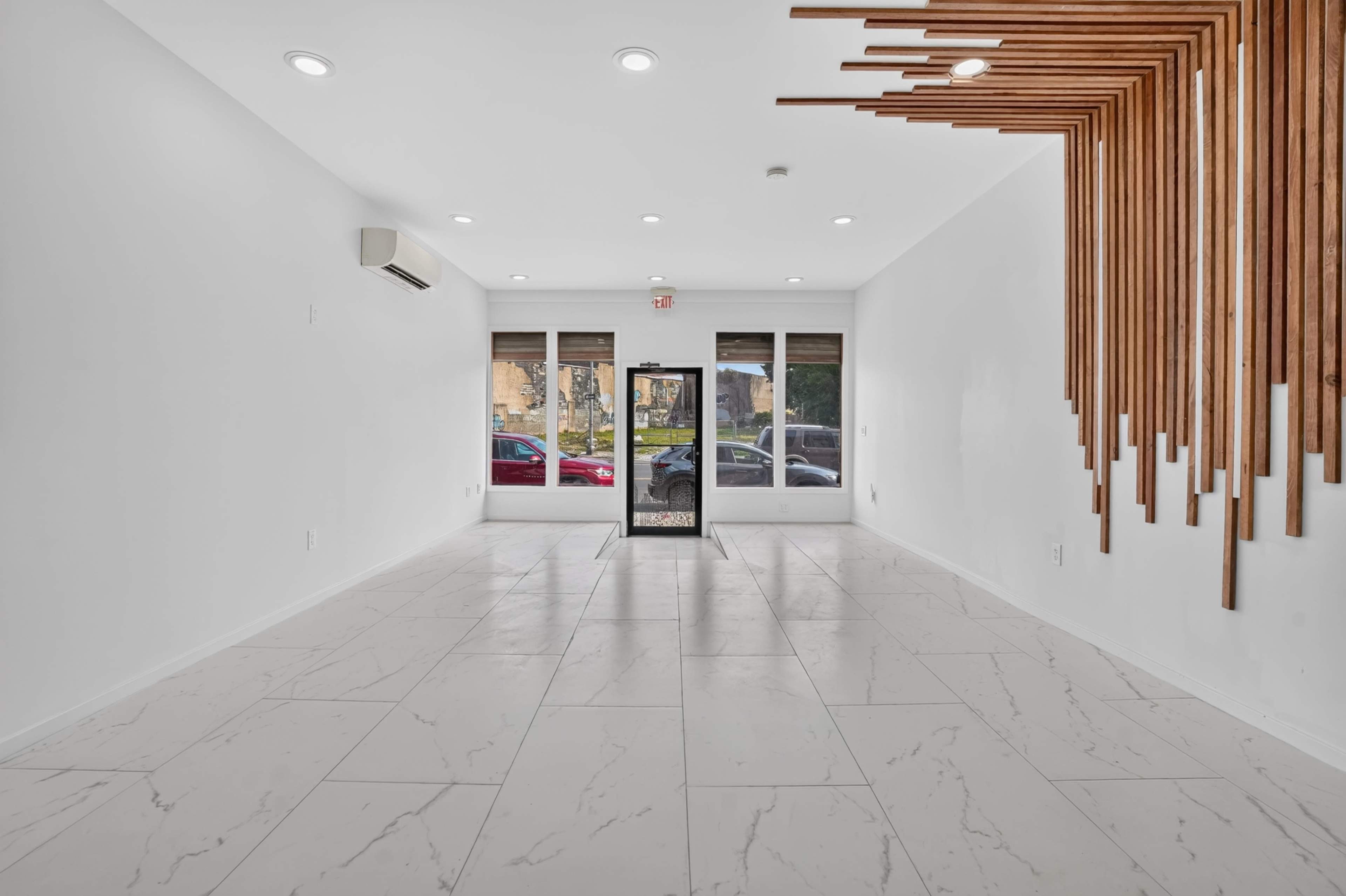 The image shows an empty, white-walled room with a marble floor and large front windows featuring a door at the center.