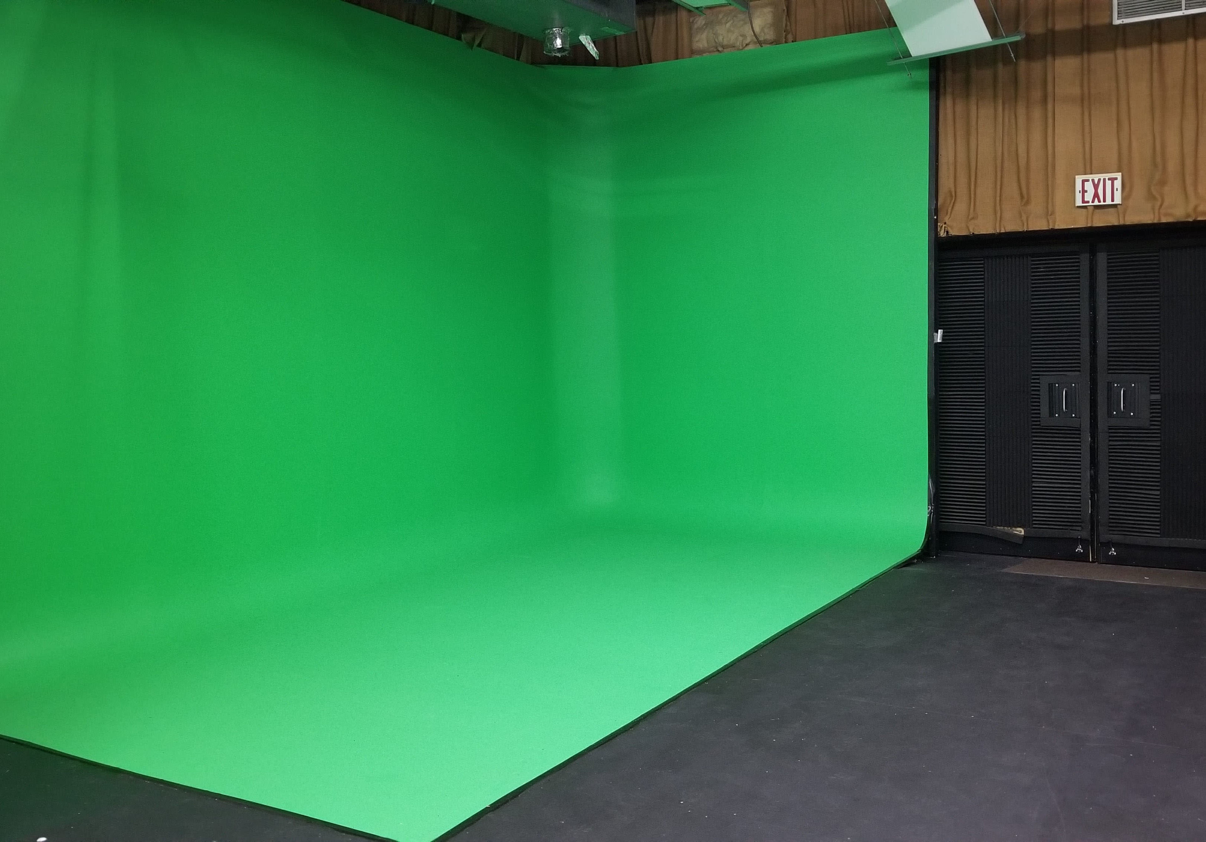 The image shows a studio space with a large green screen backdrop and dark storage doors on one side.