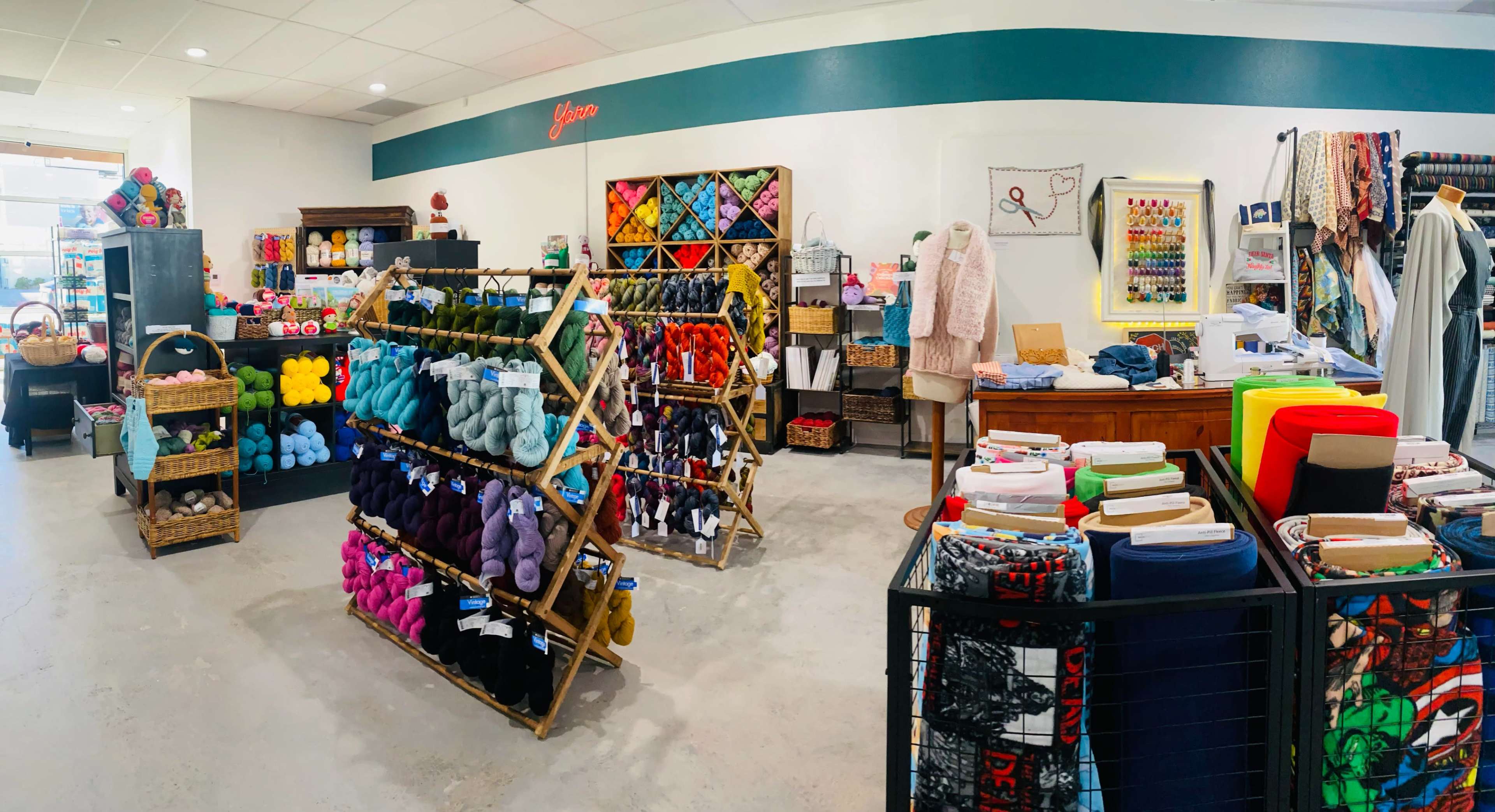 The image depicts a colorful craft store featuring shelves filled with yarn, fabrics, and various crafting supplies, organized in neat displays around a bright and inviting interior.