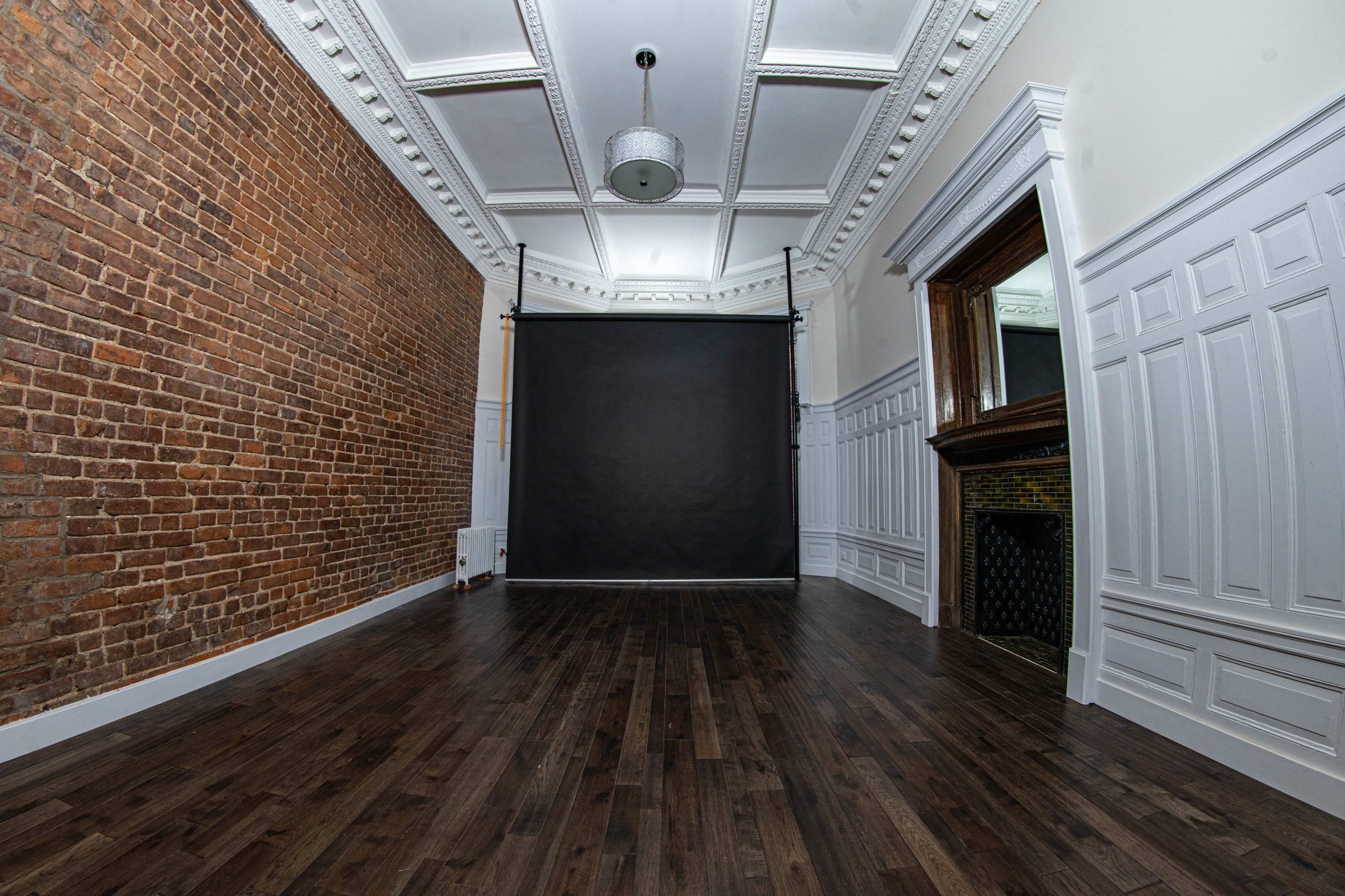 A spacious room with a brick wall, a dark backdrop, and a mirror framed by elegant moldings.
