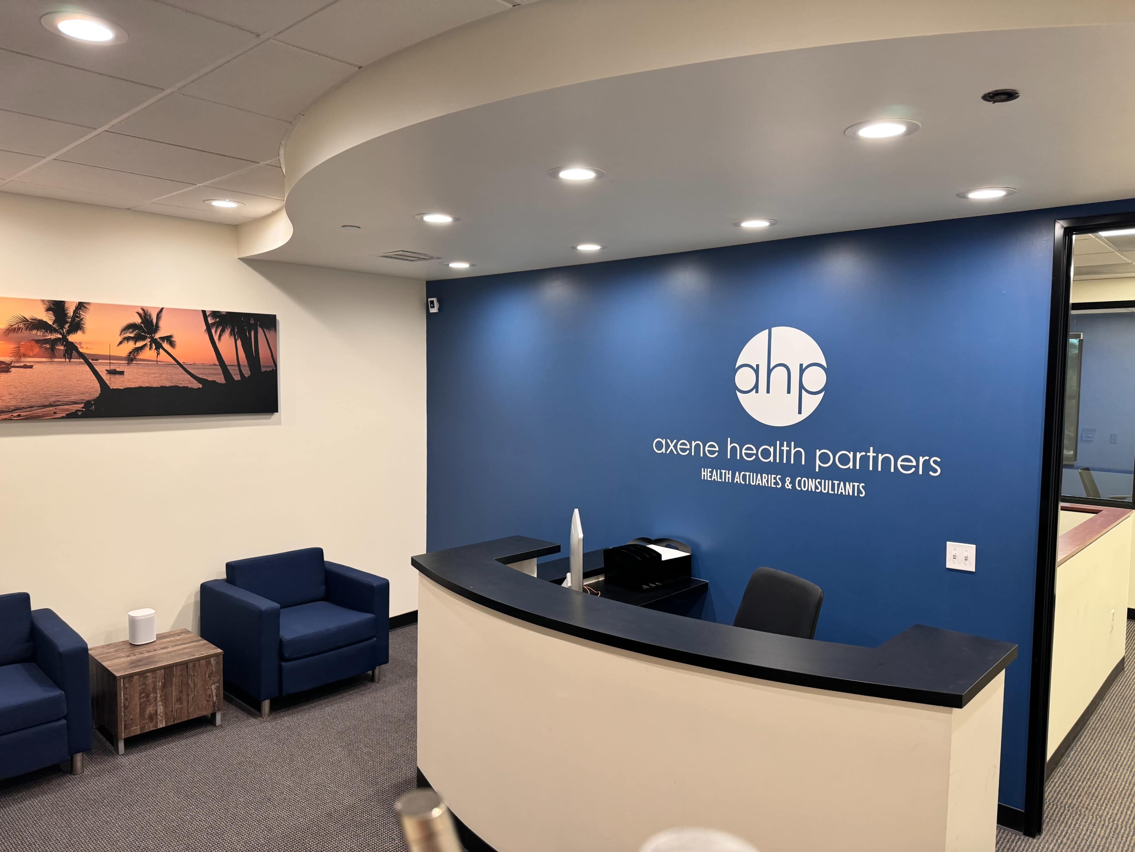 A modern office reception area with blue walls, a curved reception desk, and seating arrangements in a waiting area.