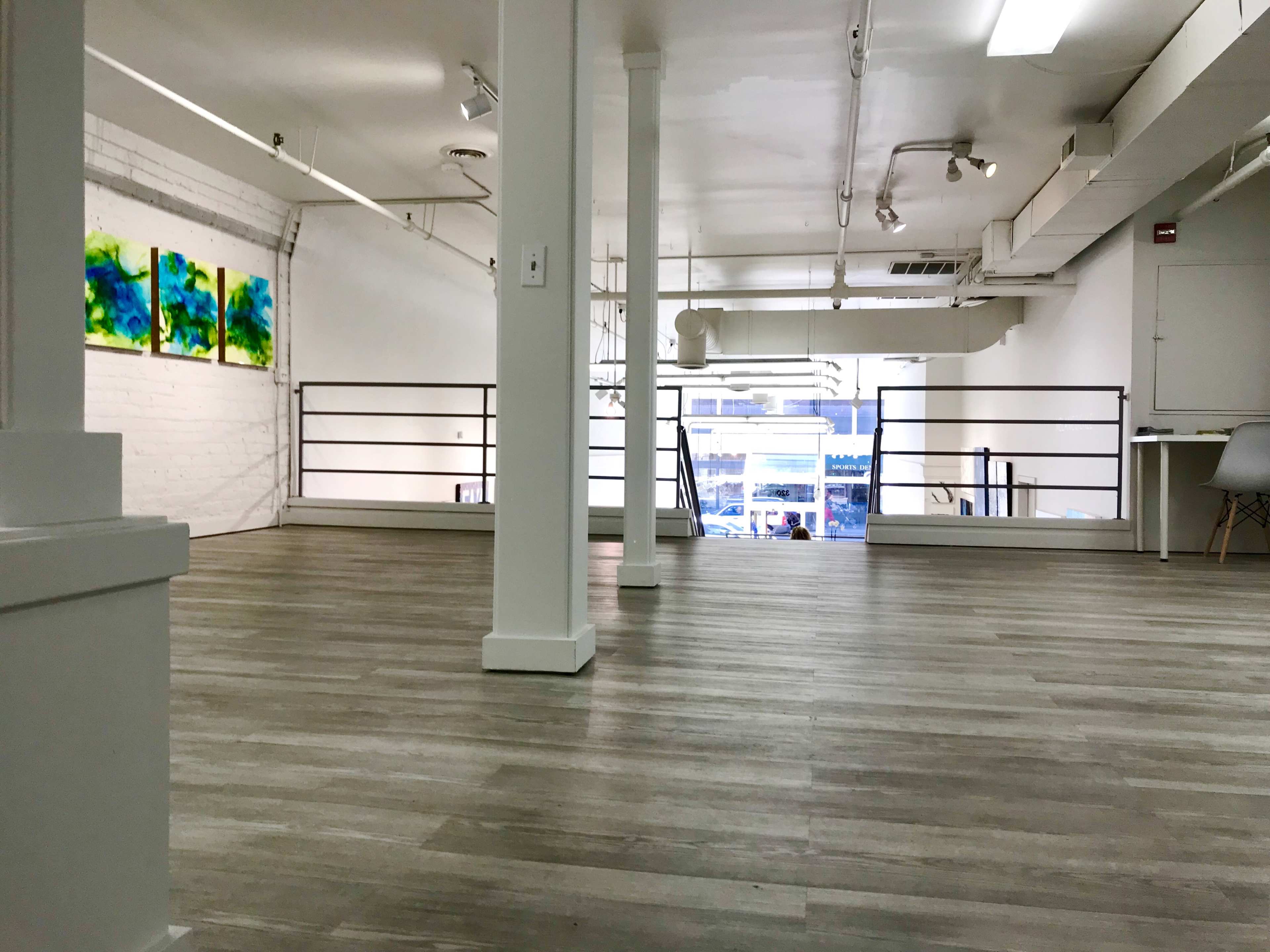 A spacious, empty loft-style room with wooden flooring, large windows, and abstract artwork on the walls.