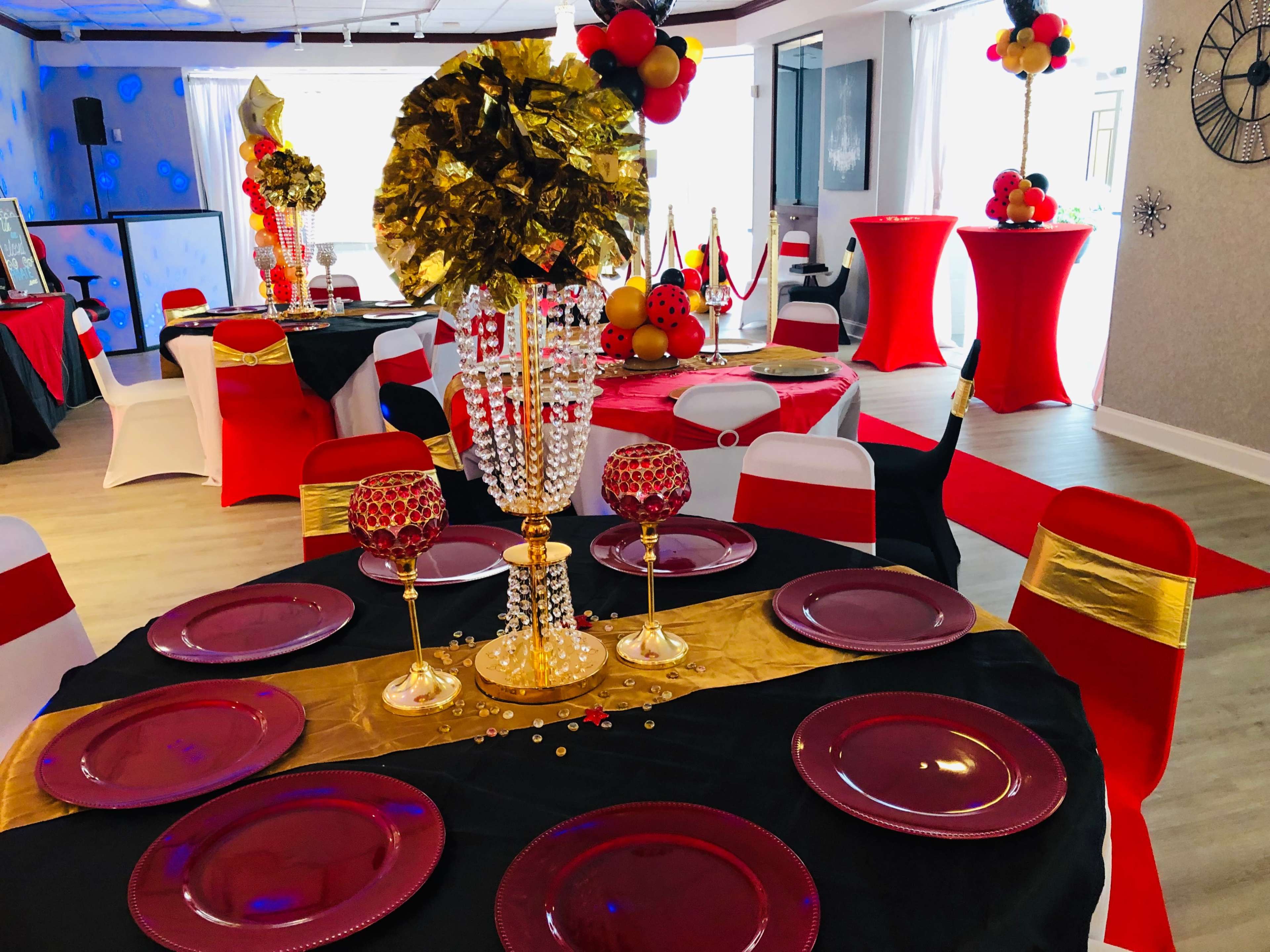The image shows a decorated banquet space with black and red table covers, elegant centerpieces, and party decor featuring gold, black, and red colors.