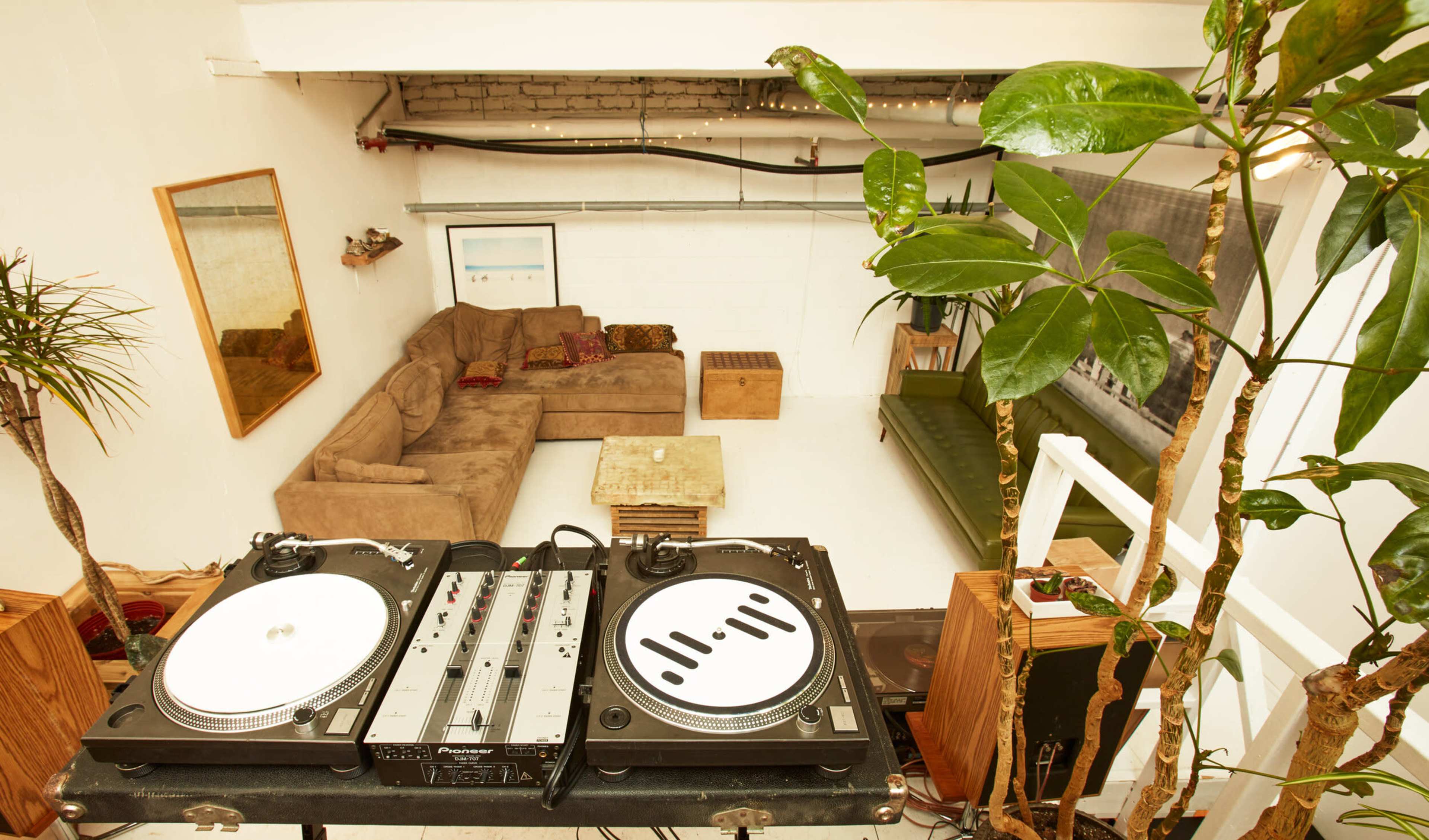 A DJ setup with turntables is positioned in front of a cozy lounge area featuring a brown couch and wooden coffee table.
