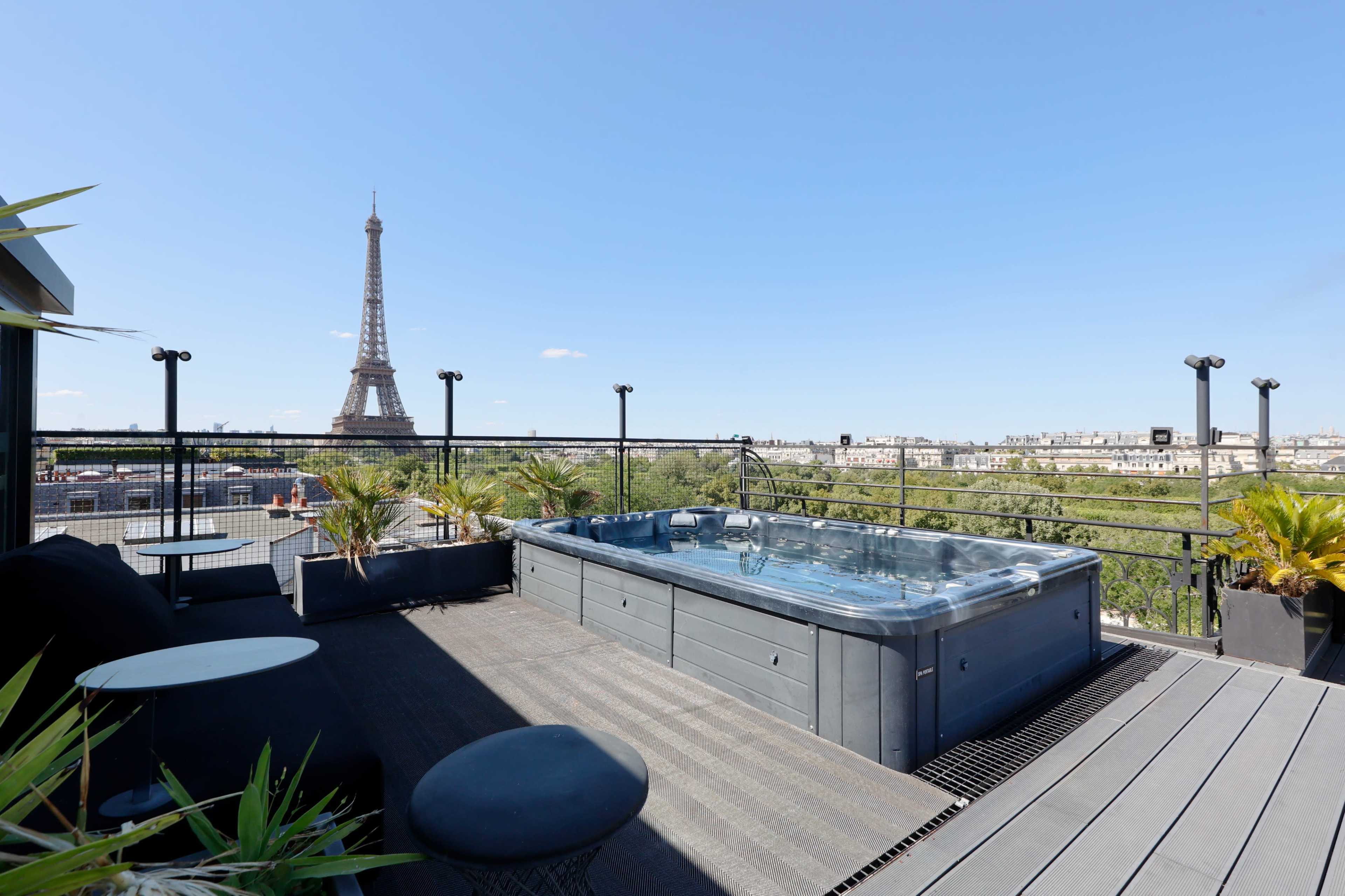 The image shows a rooftop terrace featuring a hot tub with views of the Eiffel Tower in the background.