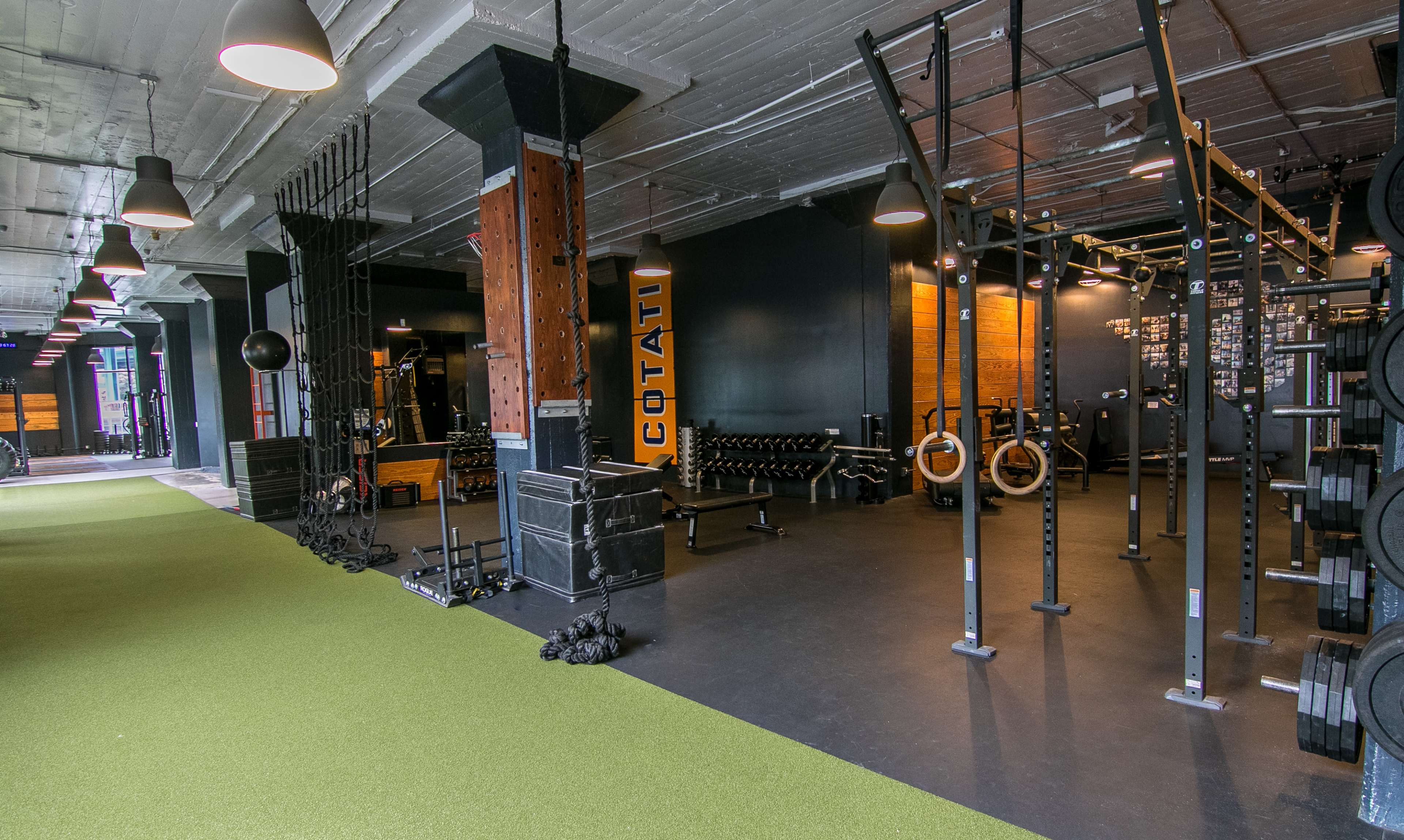 A spacious gym equipped with various fitness apparatus, including weightlifting equipment and gymnastic rings, situated on a synthetic green turf floor.