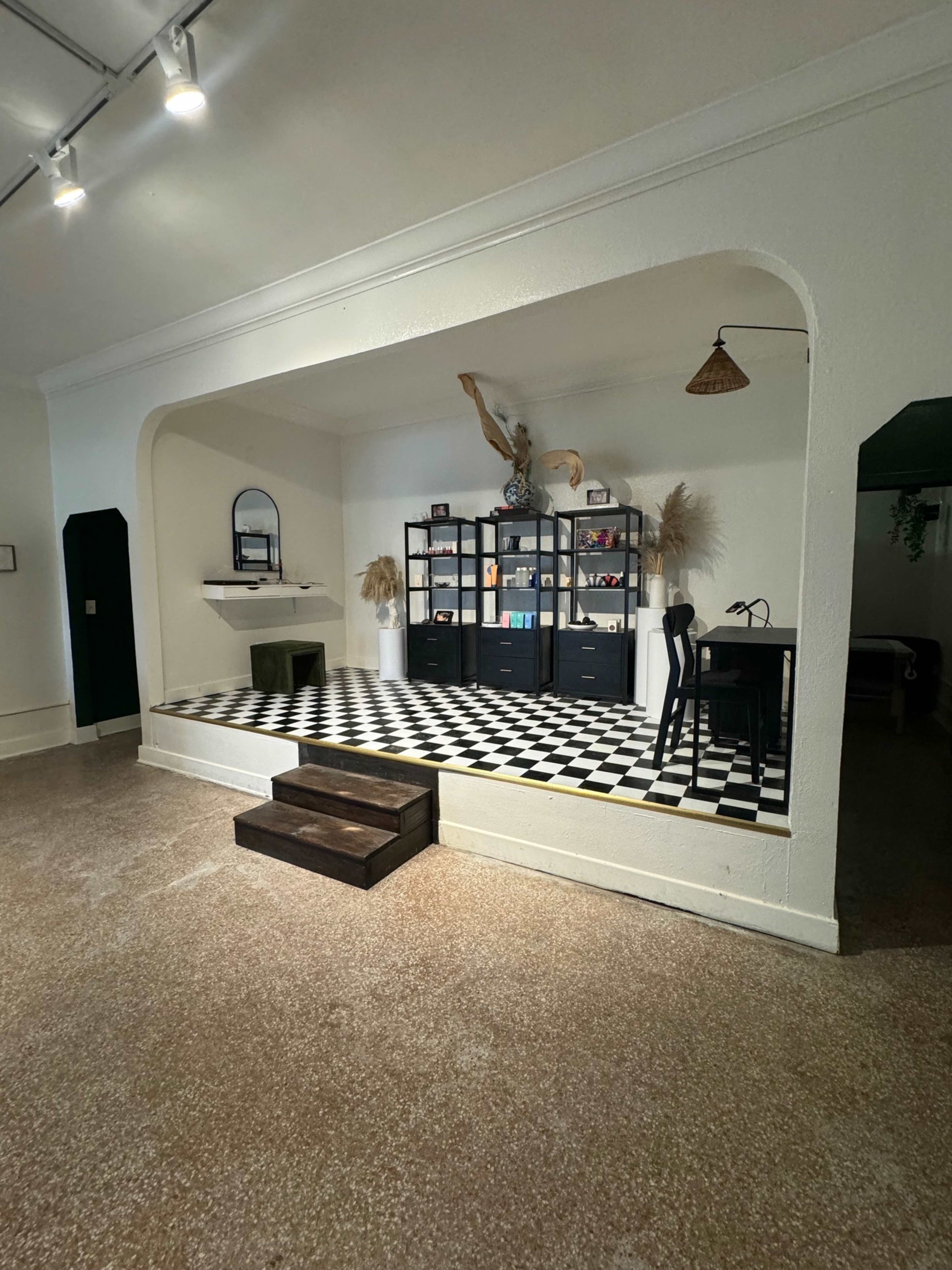 A spacious room with a raised platform featuring a black and white checkered floor, a shelf of decorative items, and a small desk.