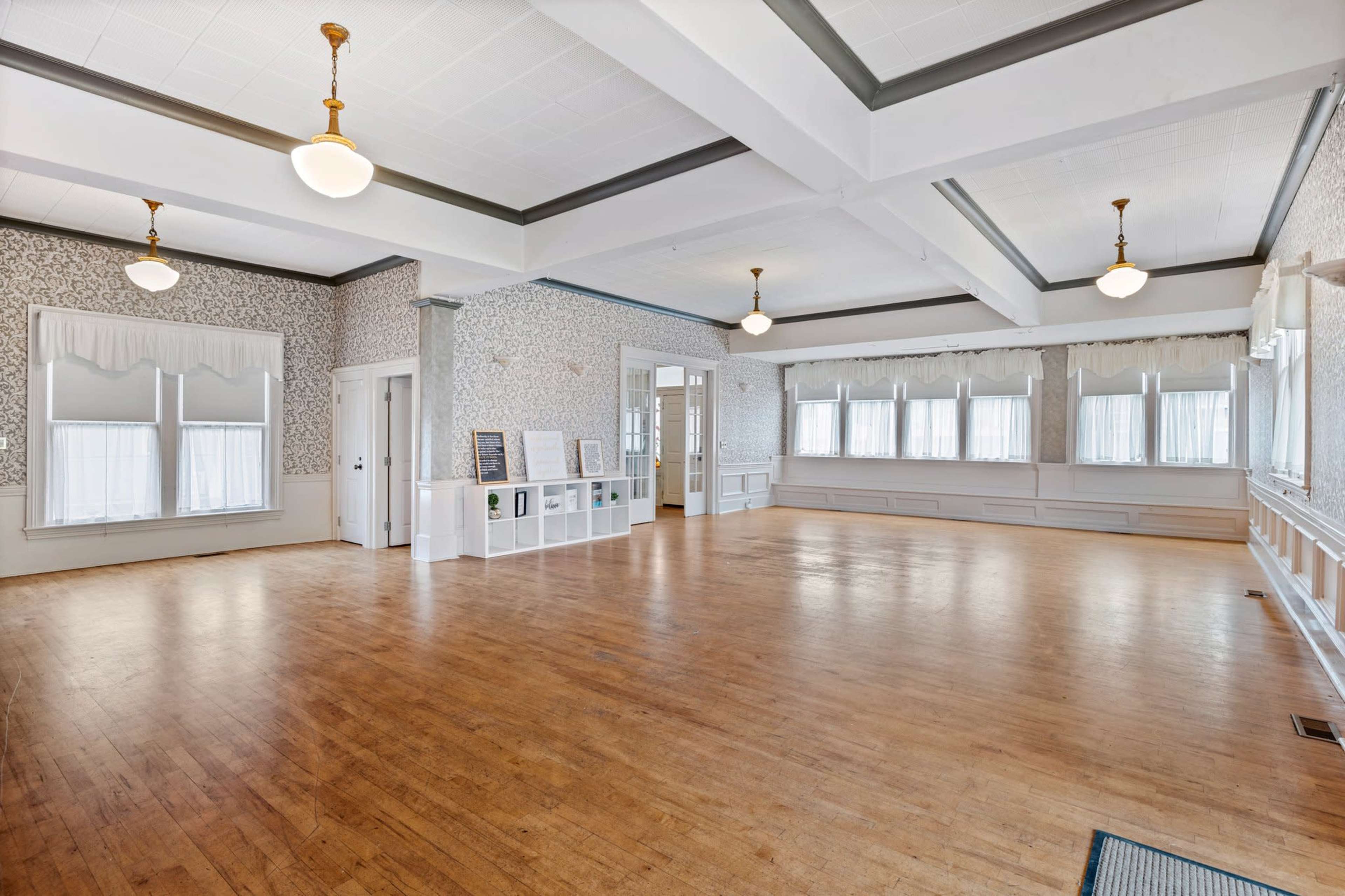 A spacious, empty room with wooden floors, large windows, and decorative wall detailing.