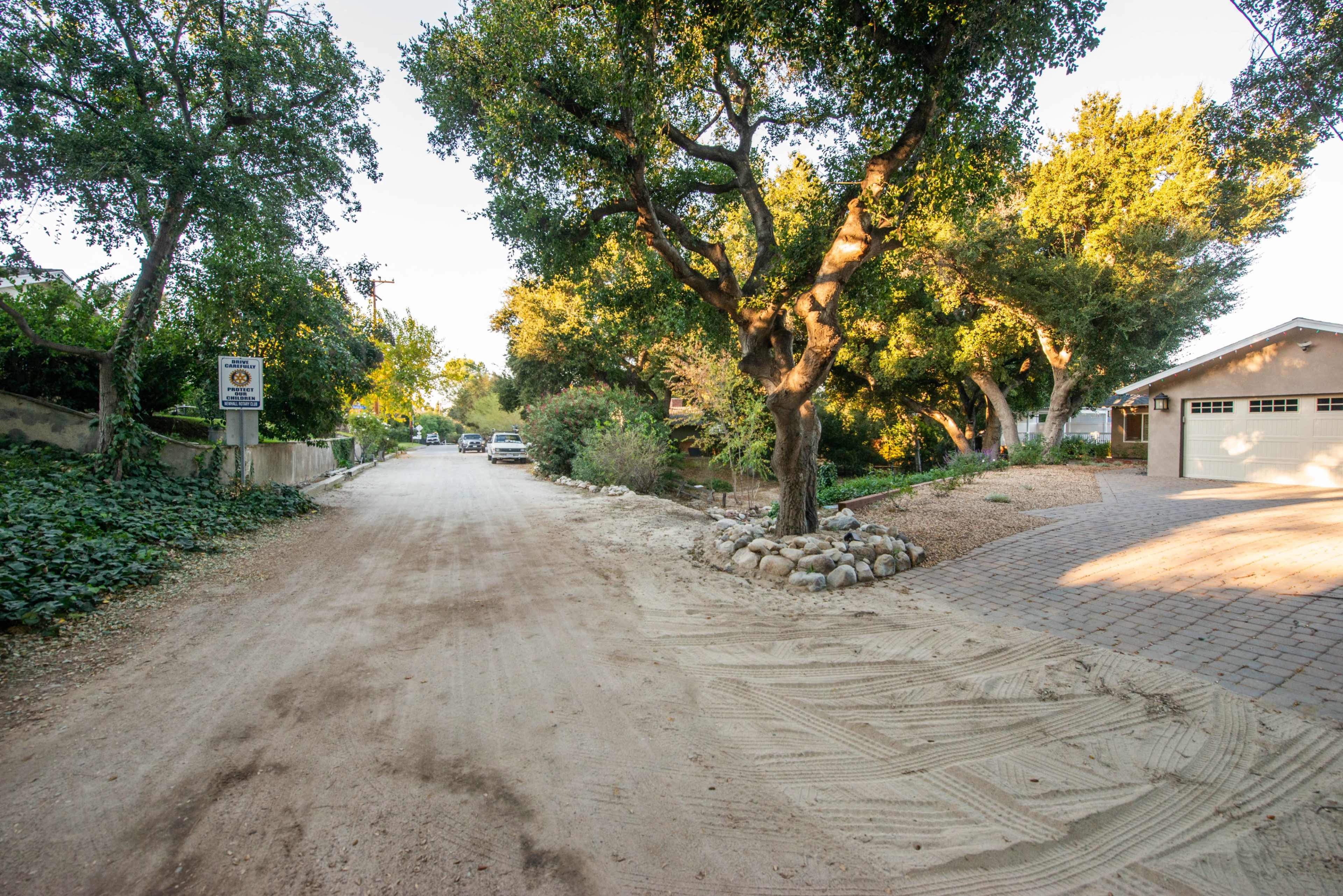 A dirt road lined with trees leads to a house with a paved driveway on the right.