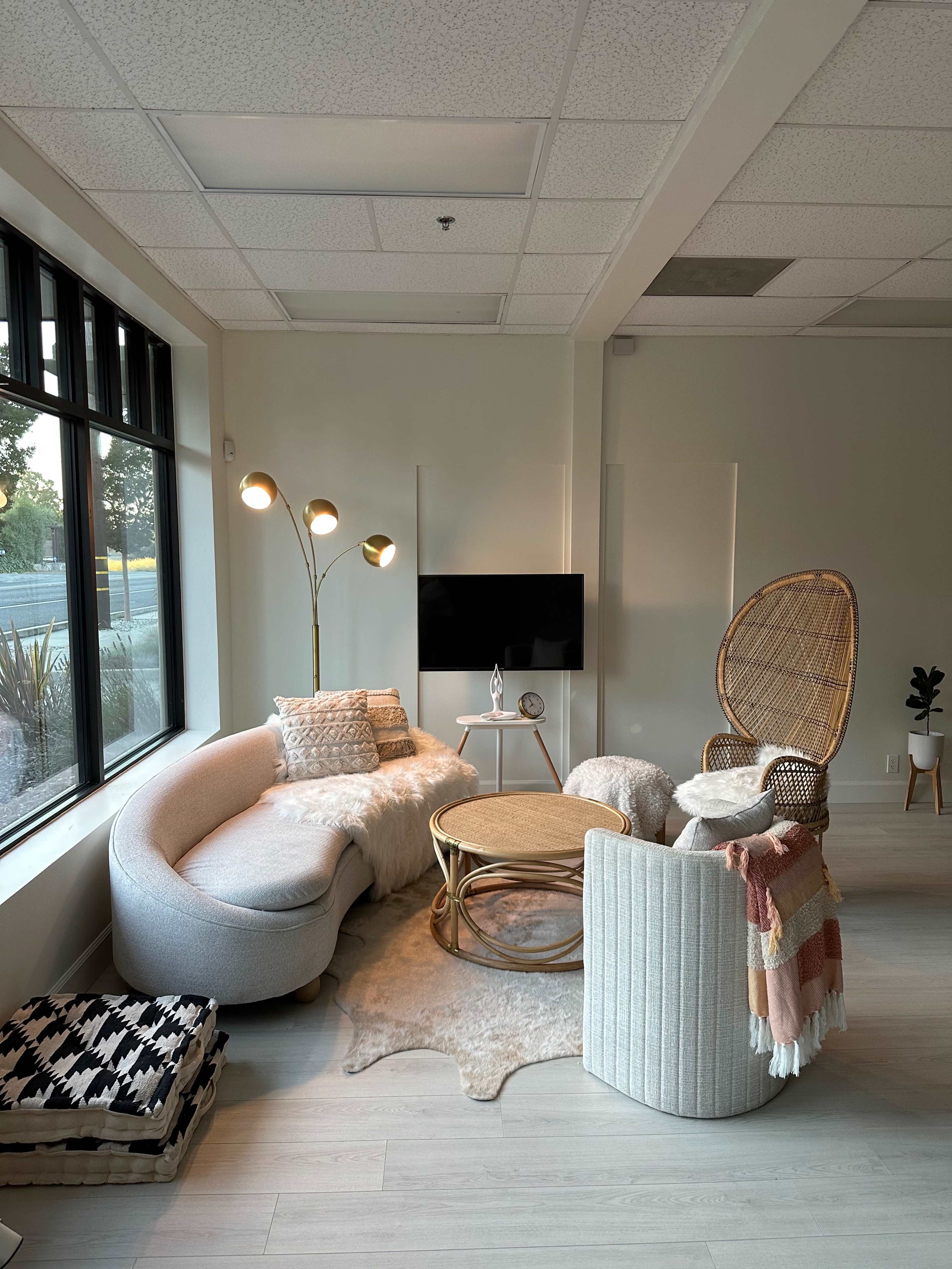 A modern living room with a curved sofa, a round coffee table, a rattan chair, and a floor lamp, all set near a window.