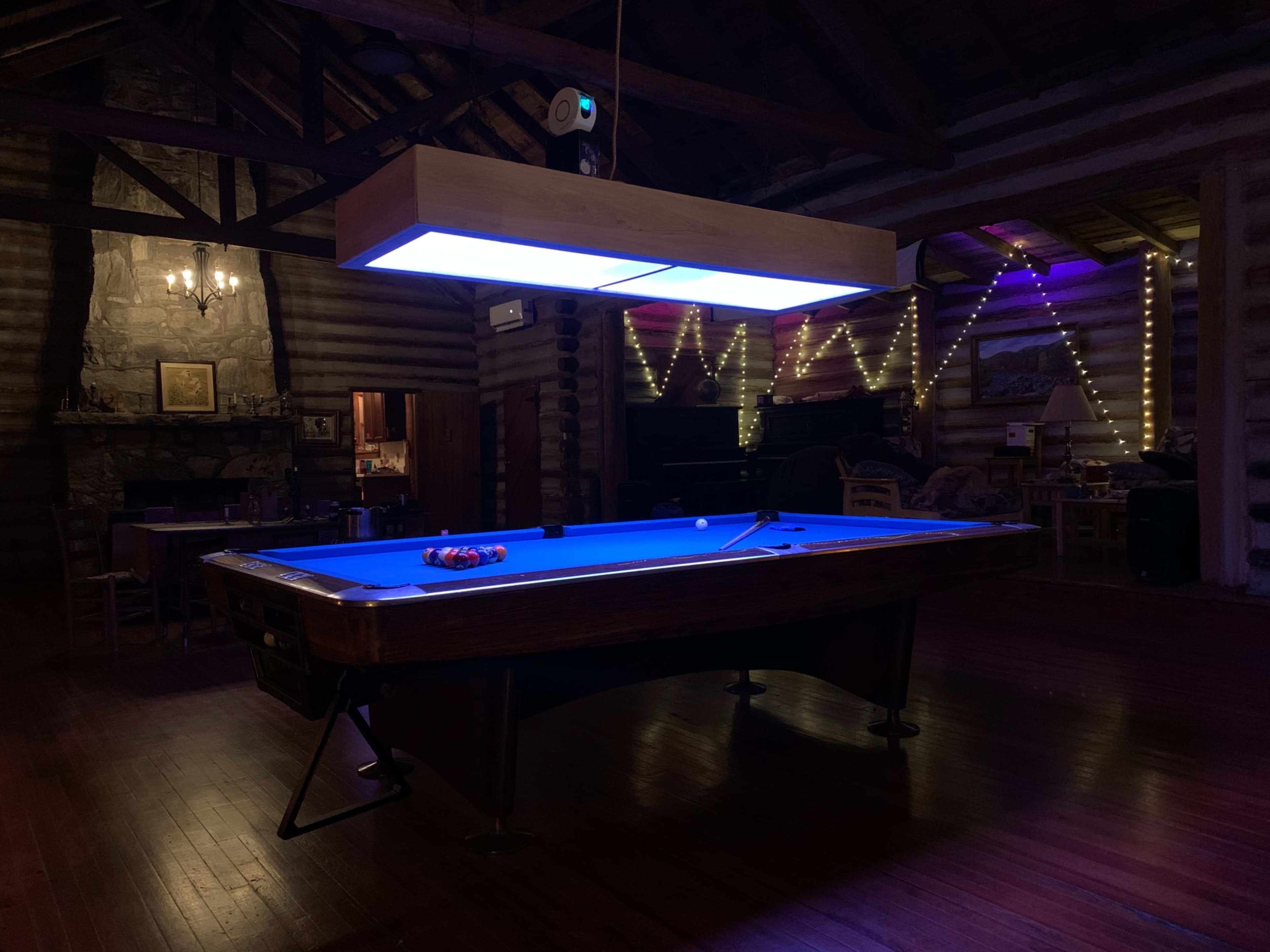 A lit pool table sits in the center of a wooden room featuring exposed beams and stone accents.