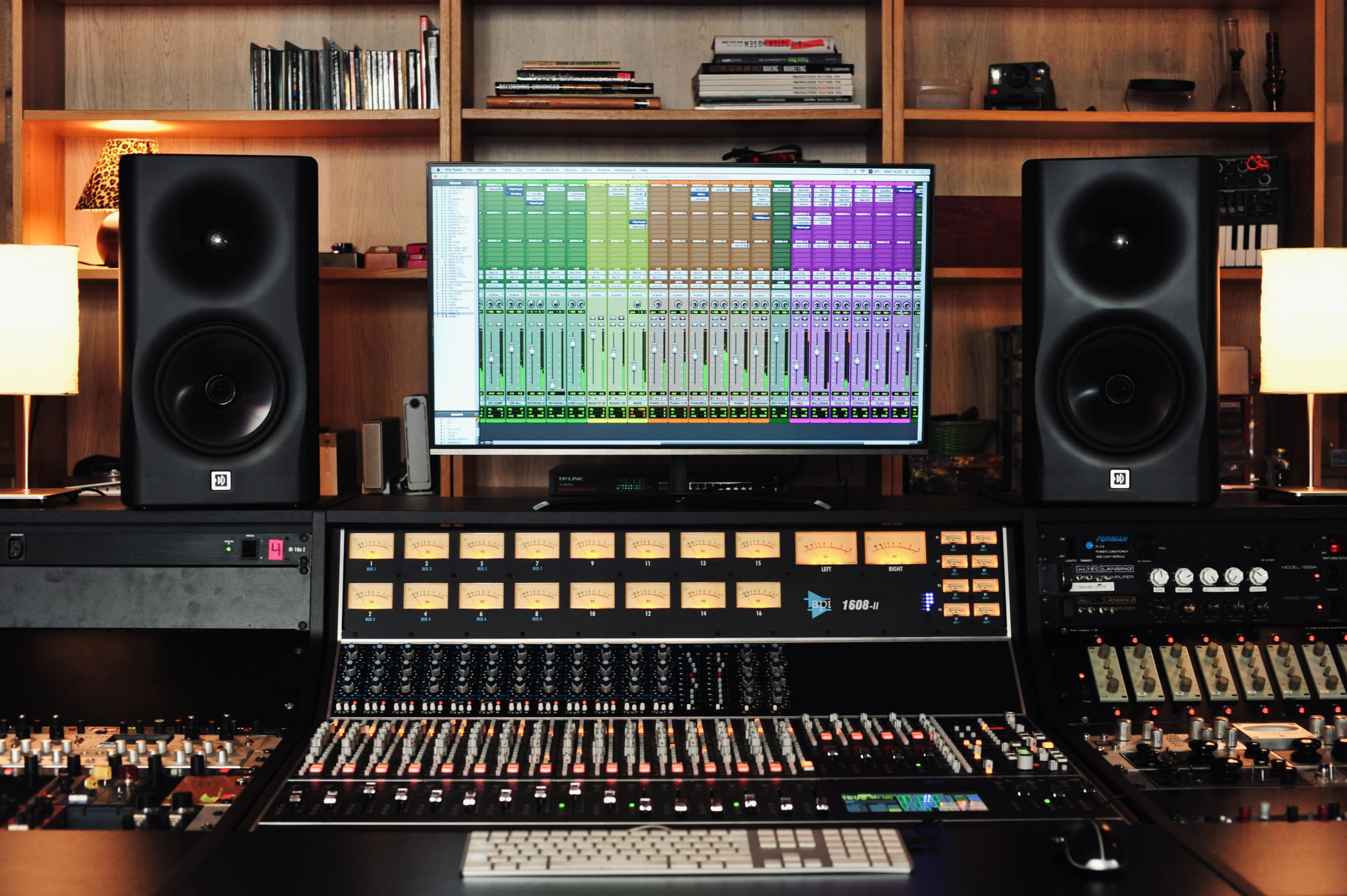 A music studio setup features a large mixing console, studio monitors, and a computer screen displaying audio tracks.