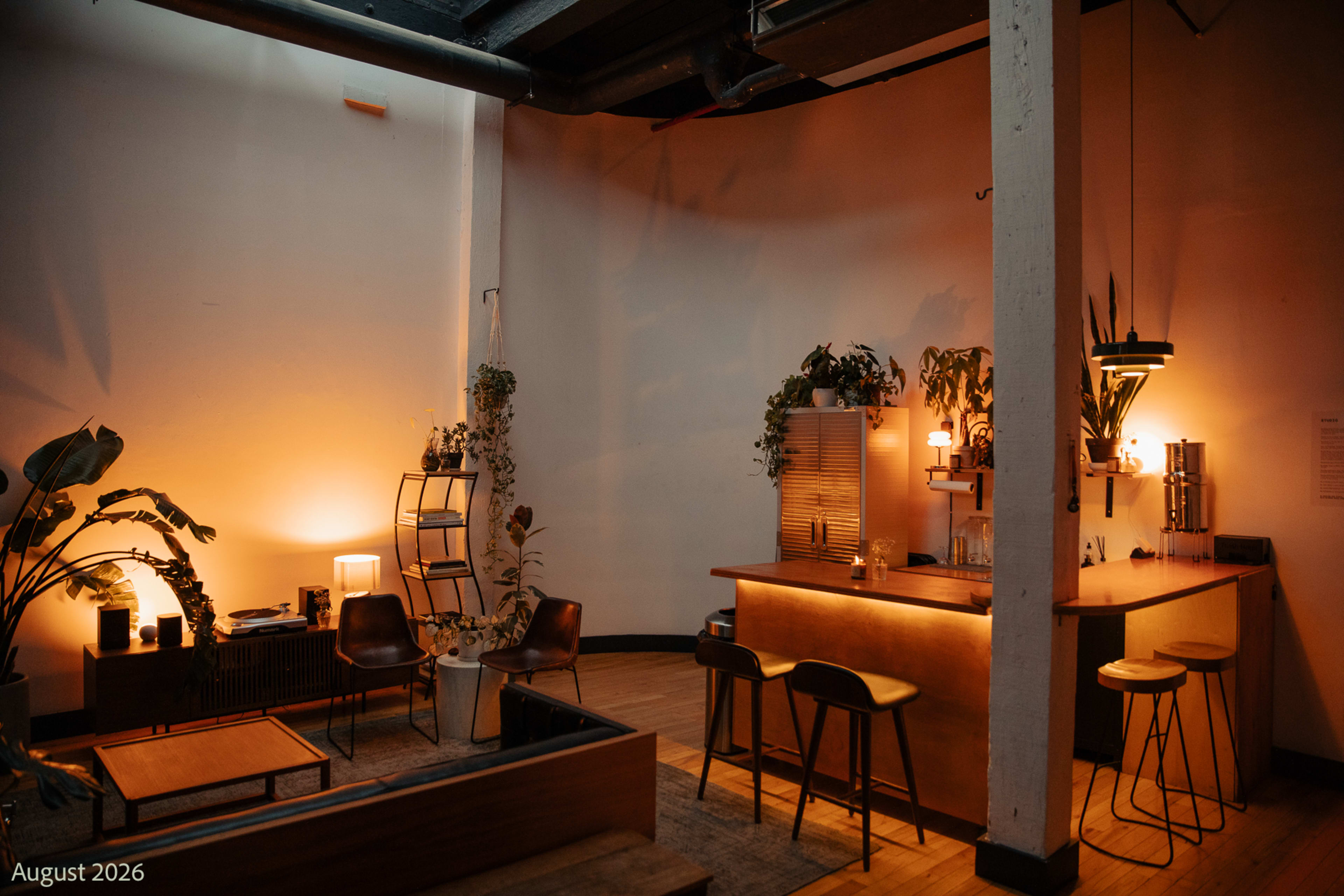 The image shows a dimly-lit interior space with a bar area, seating, and various plants arranged around a warm ambiance.