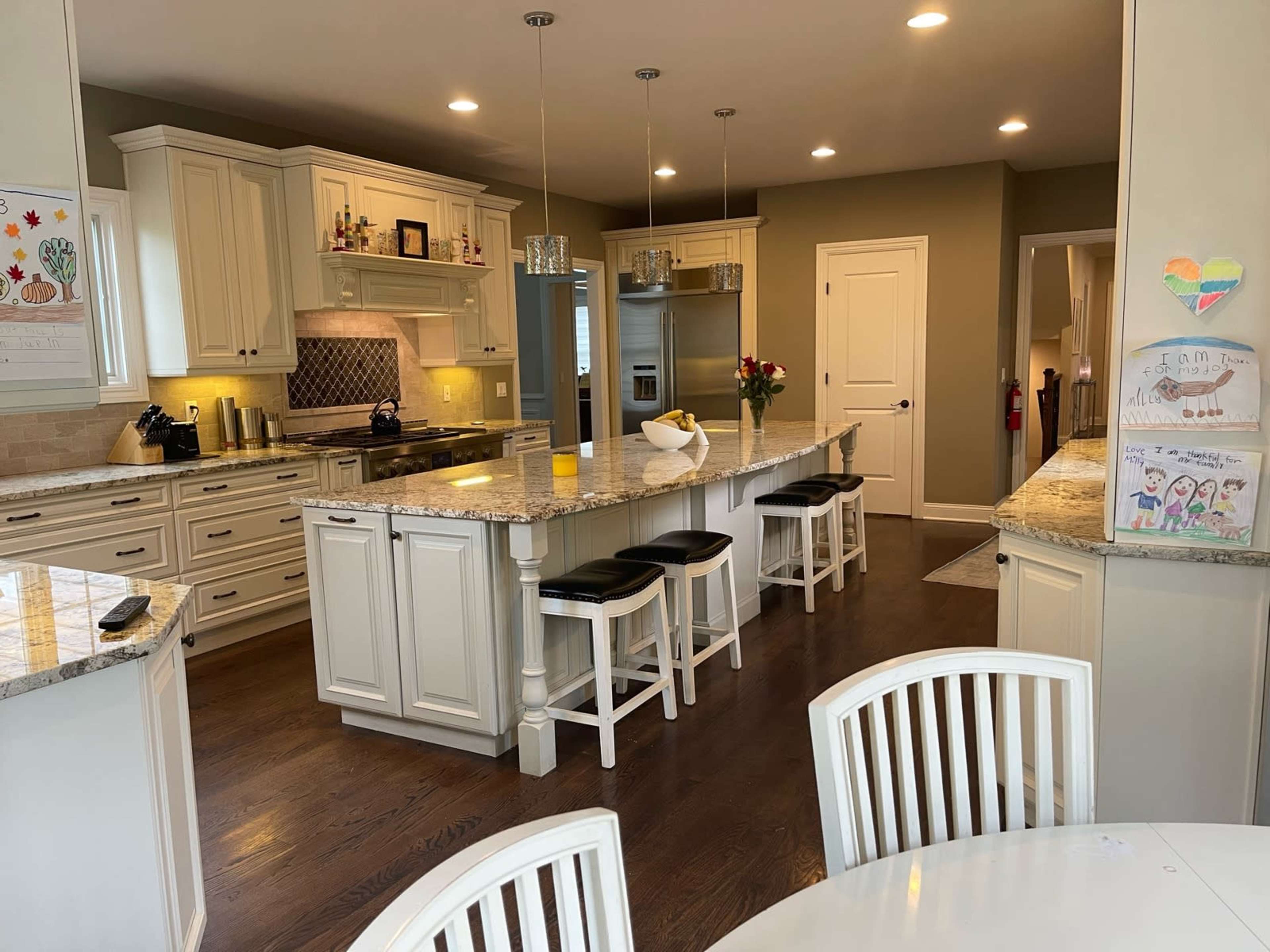 The image shows a modern kitchen with white cabinetry, a large island with bar stools, and a dark hardwood floor.