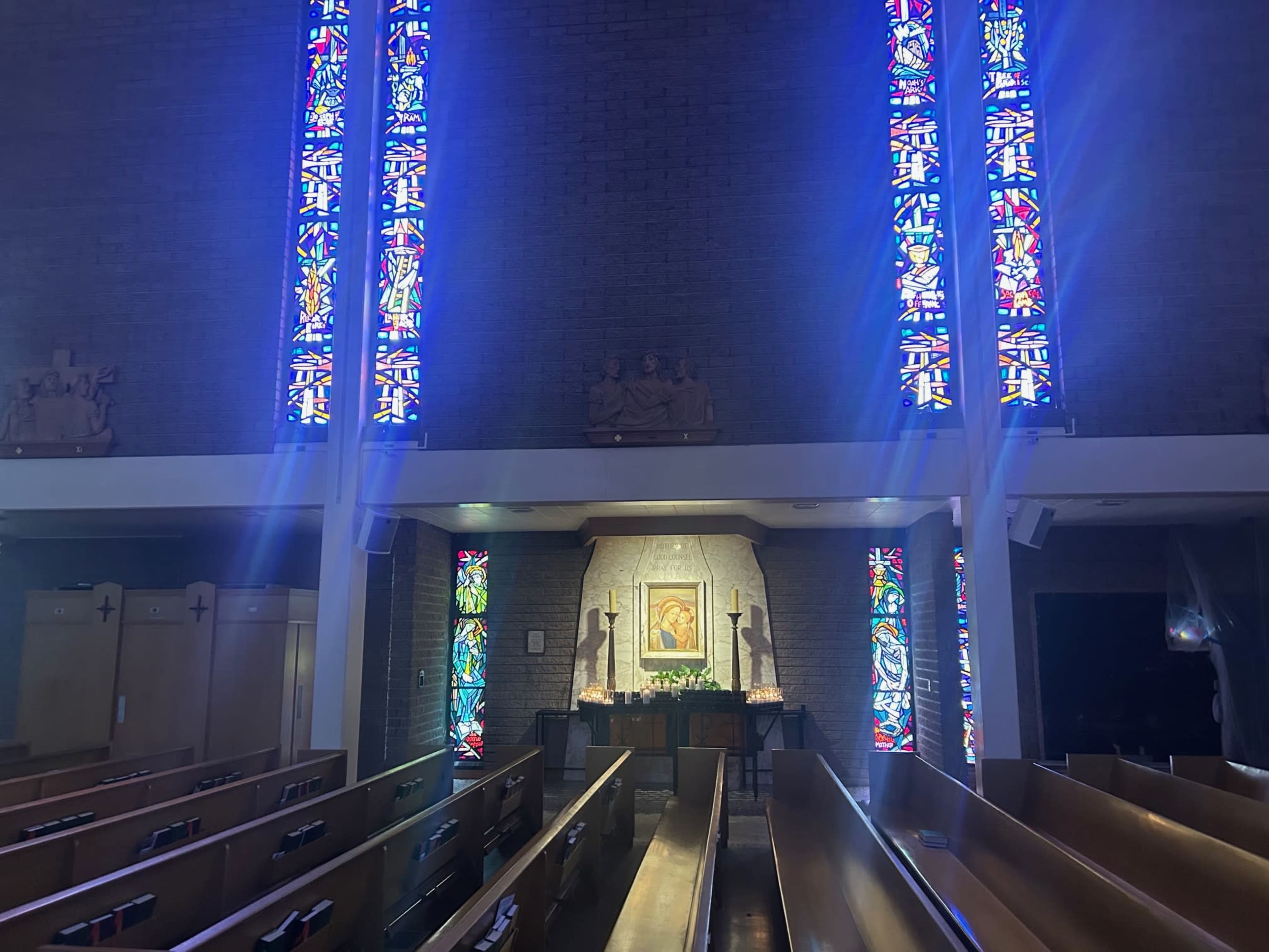 The image shows the interior of a church with stained glass windows illuminating the altar area, and rows of wooden pews in the foreground.
