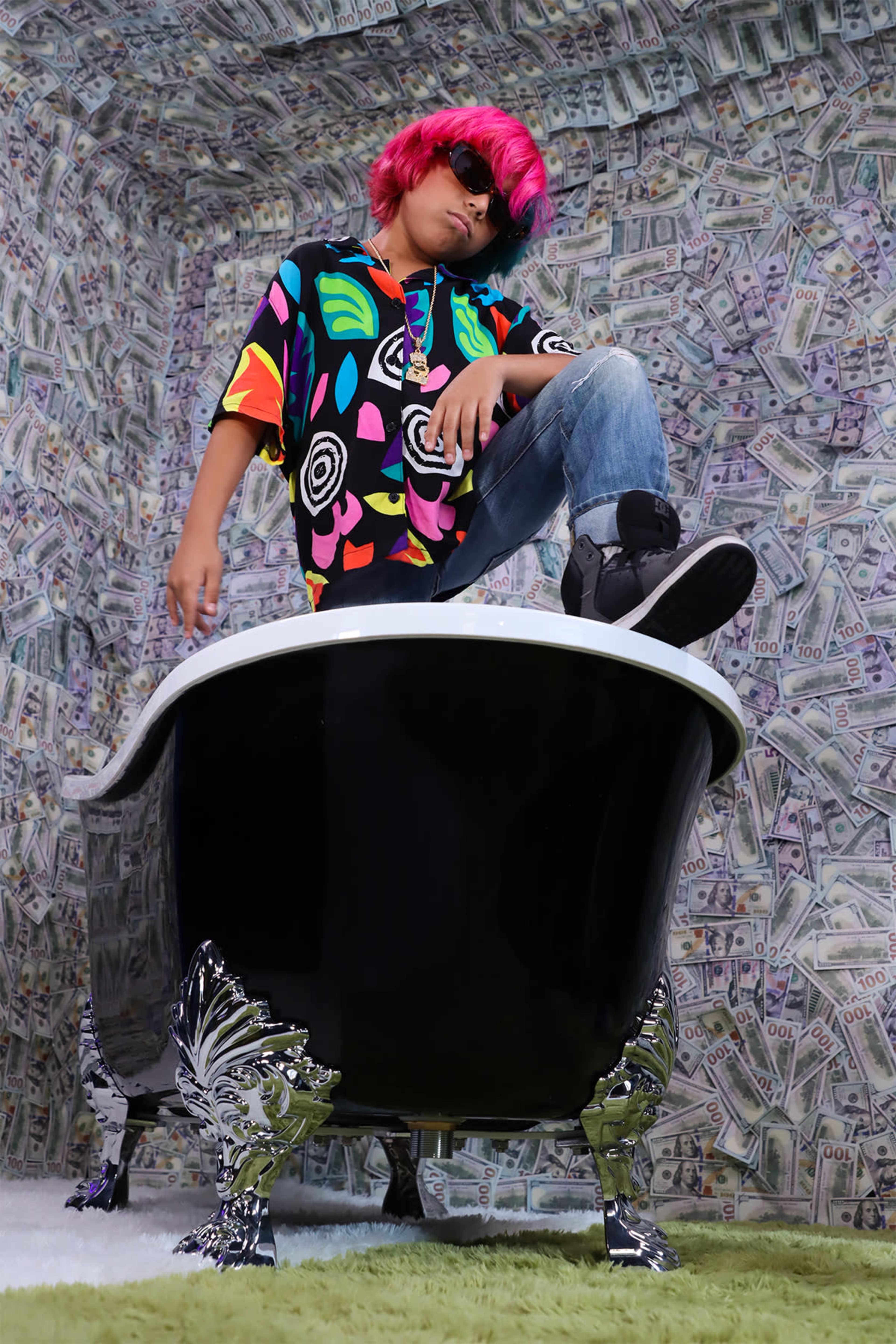 A person with pink hair stands in a black bathtub surrounded by a wall covered in images of money.