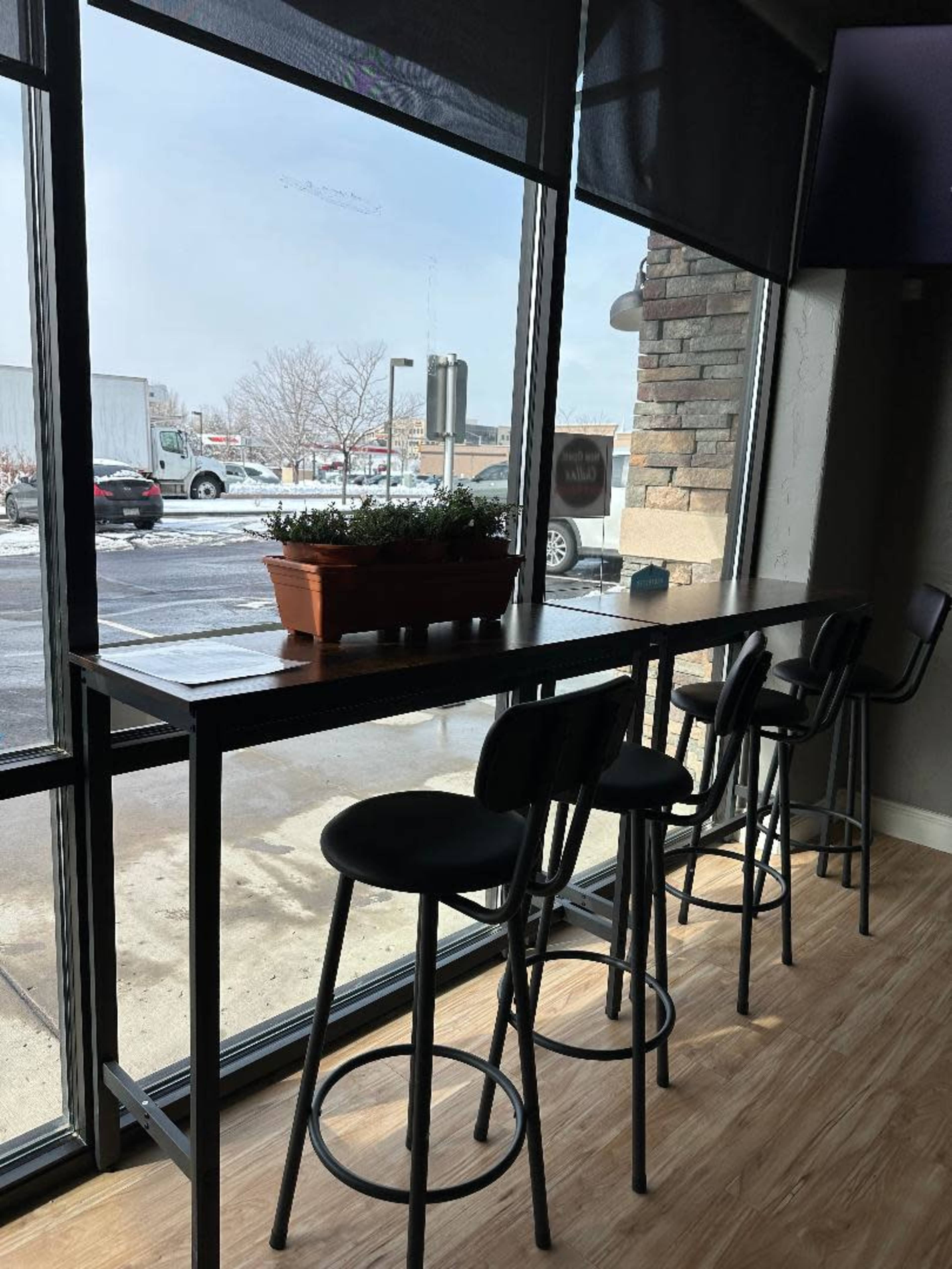 A long table with bar stools is positioned by large windows, overlooking a snowy outdoor scene.