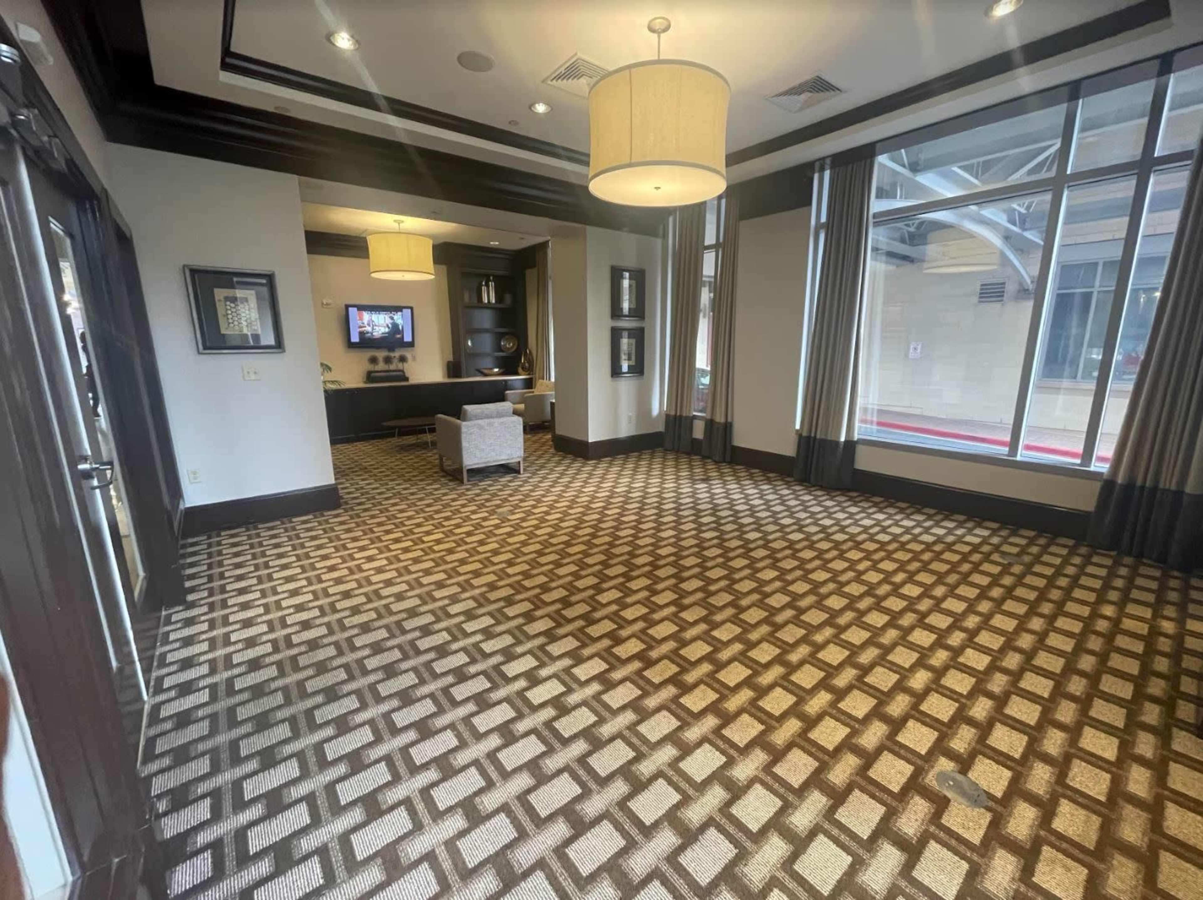 A spacious lobby area featuring a patterned carpet, large windows, and a small seating arrangement.