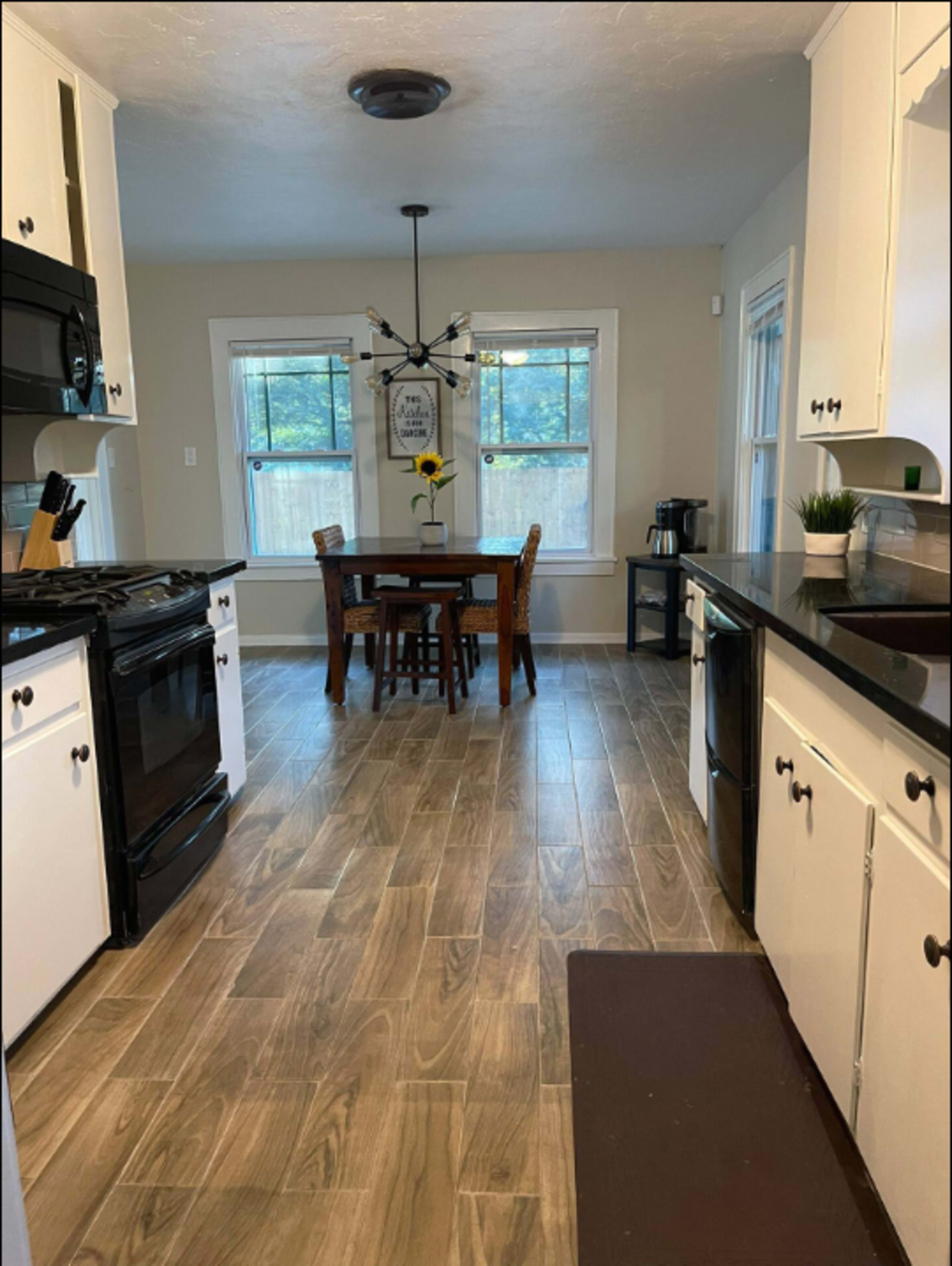 A kitchen with white cabinets, a black countertop, and a dining table with four chairs near two windows.