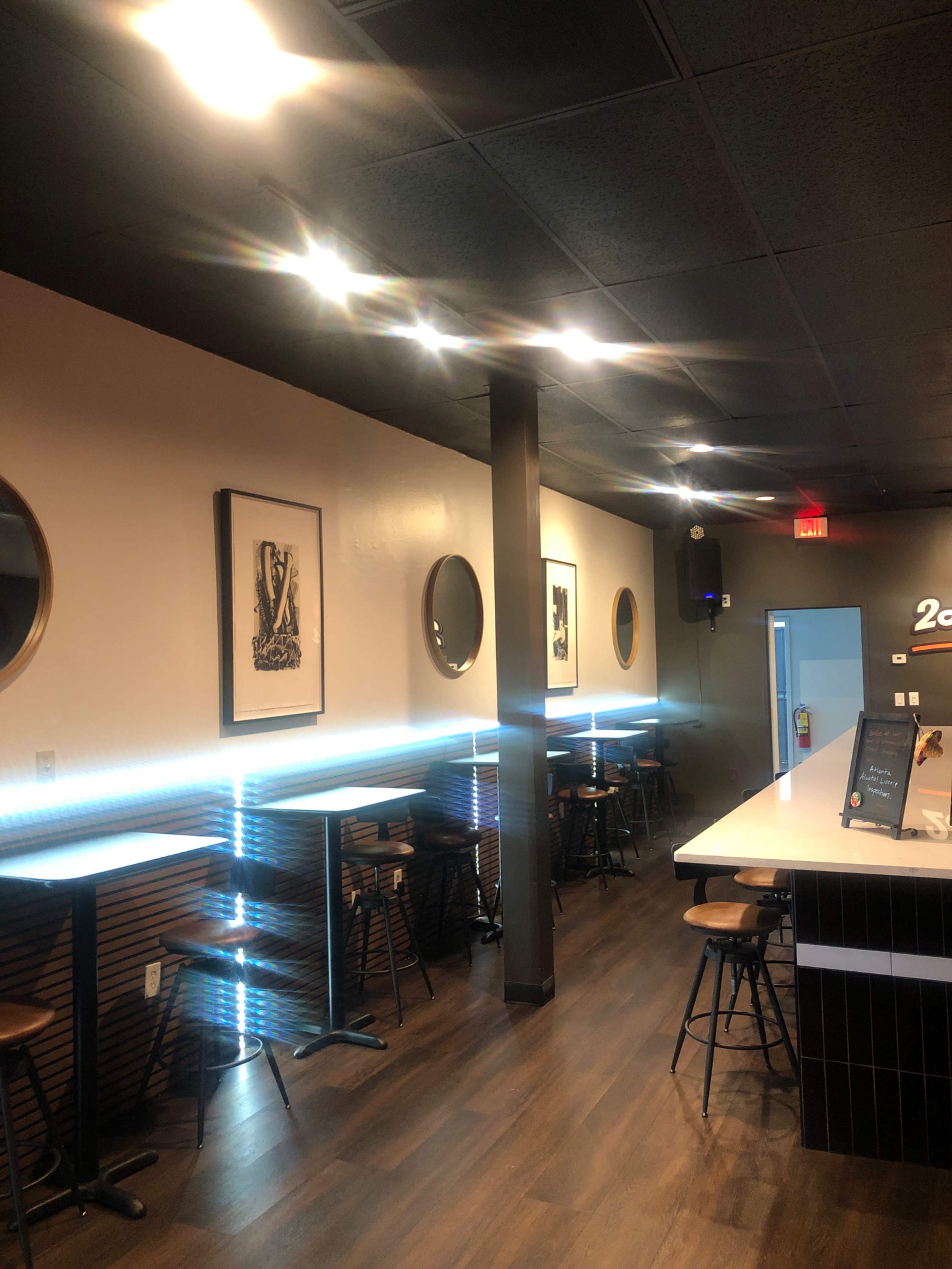 The image shows a modern café or bar interior with framed artwork on the walls, circular mirrors, and a sleek counter illuminated by blue lighting.