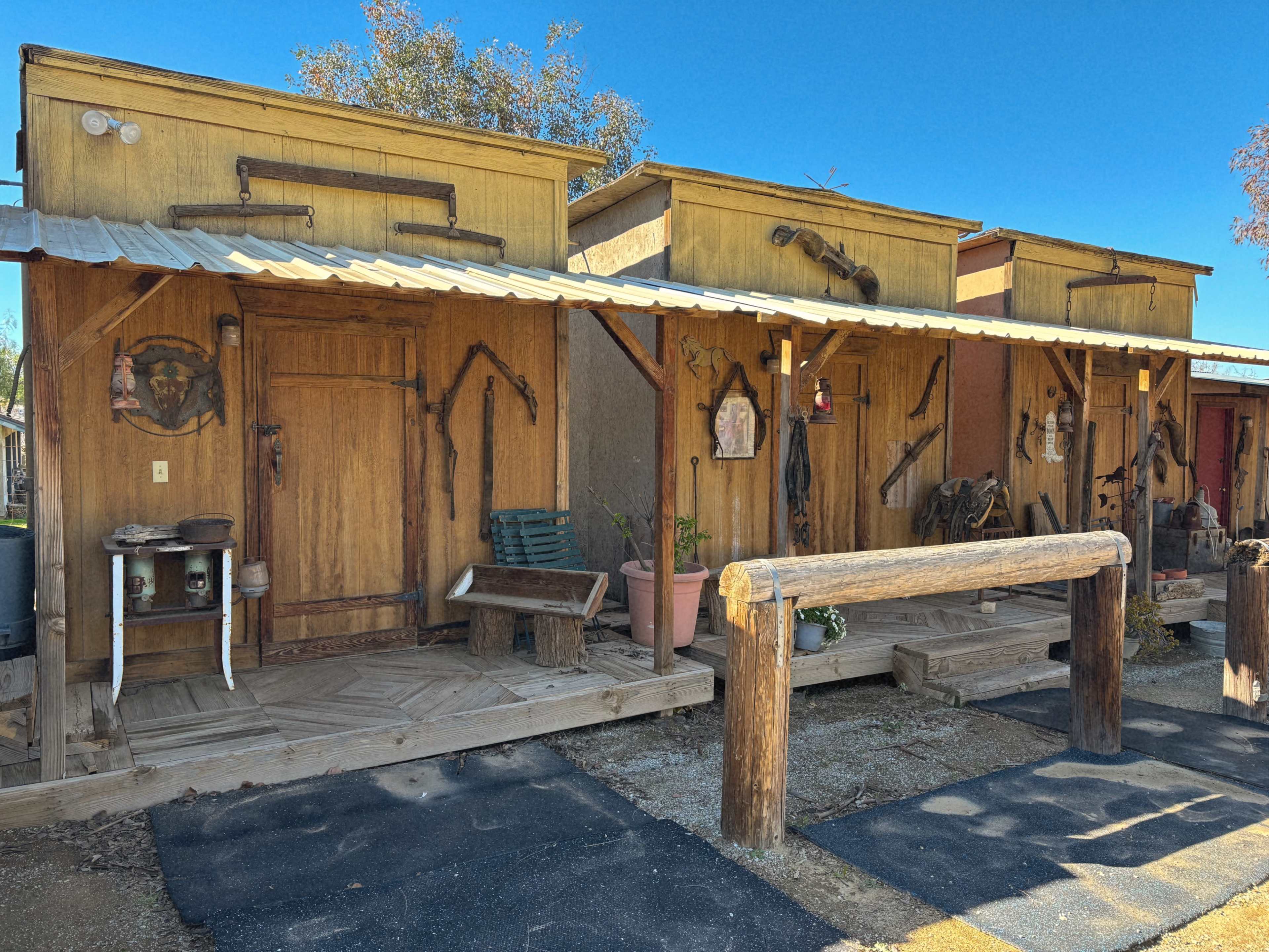 A row of rustic wooden cabins with a porch, each featuring various tools and decorations on the walls.
