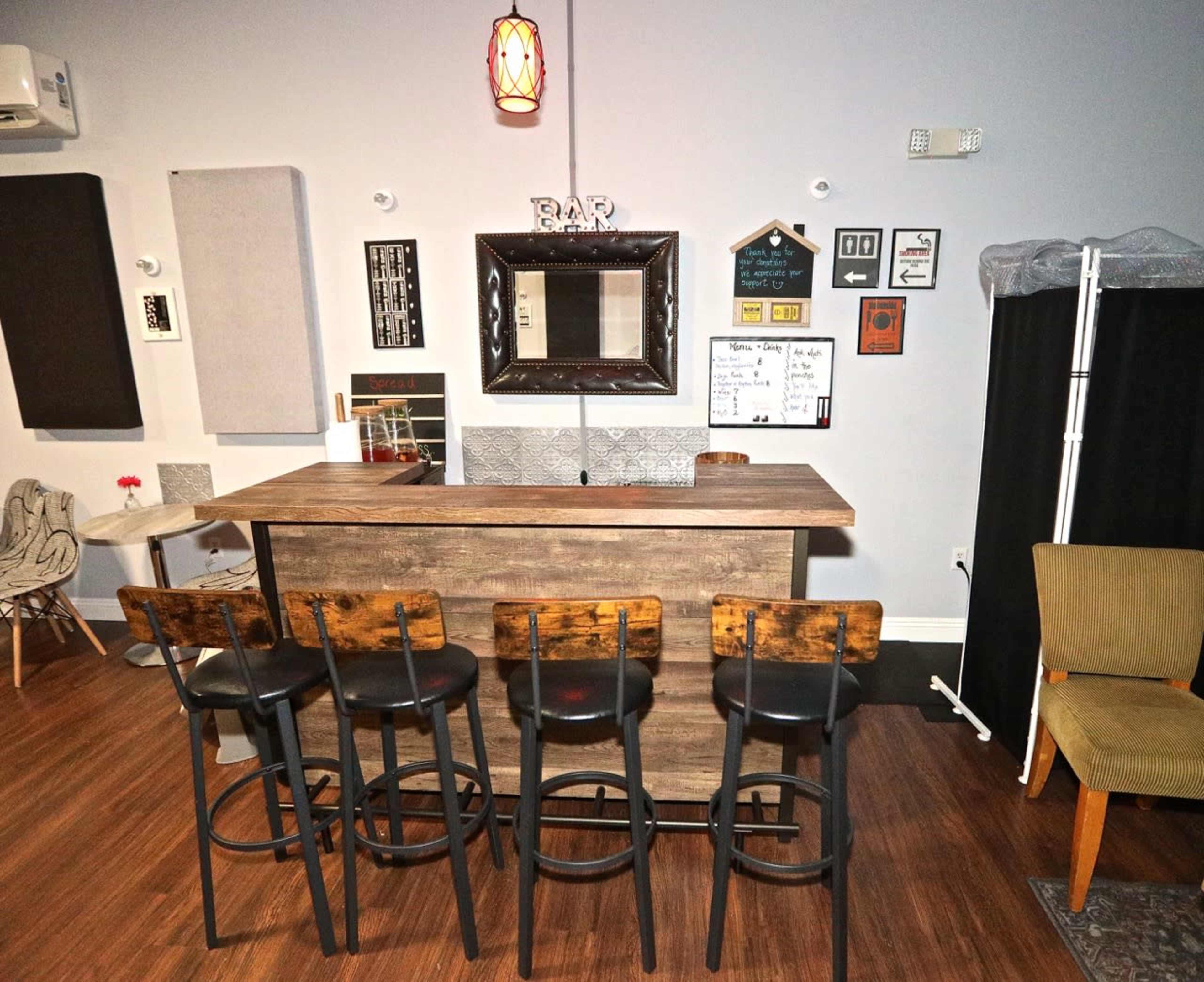 A modern bar area with a wooden counter and five black stools arranged in front of it, surrounded by various wall decorations.