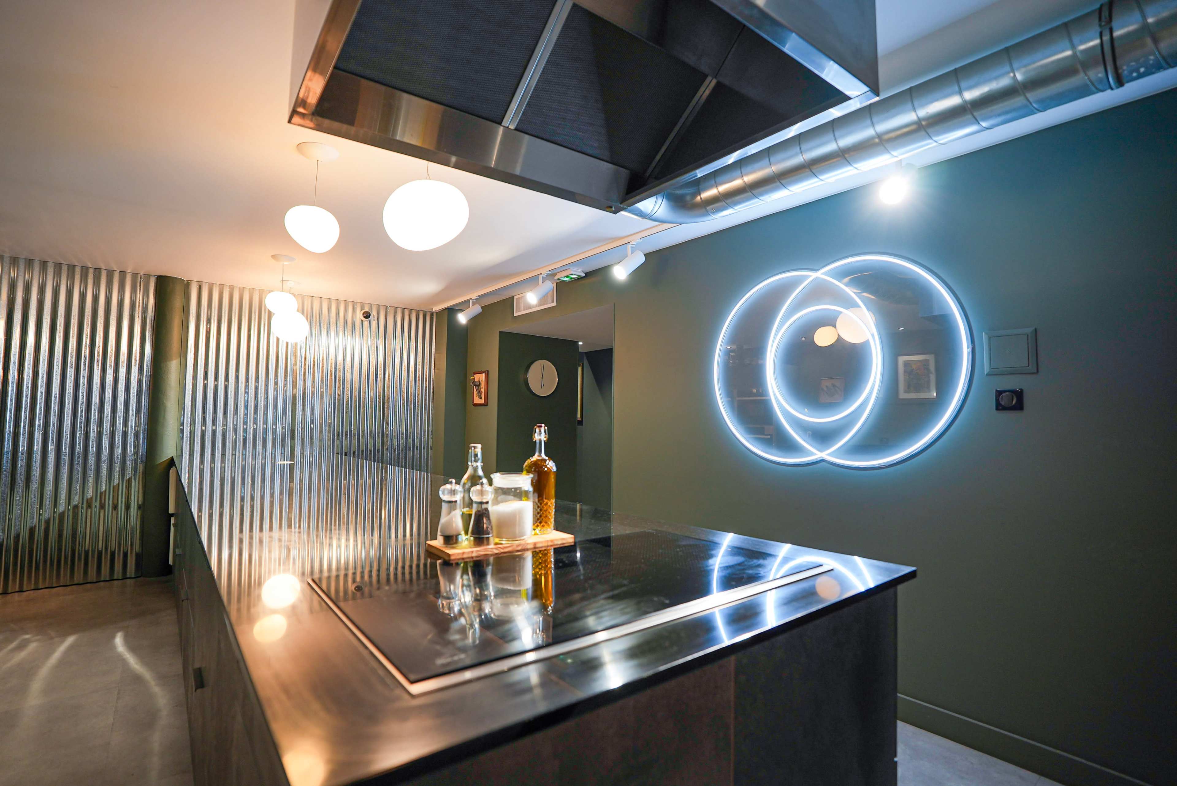 The image shows a modern bar area featuring a sleek countertop, illuminated bottles on a tray, and a wall with circular neon lights.