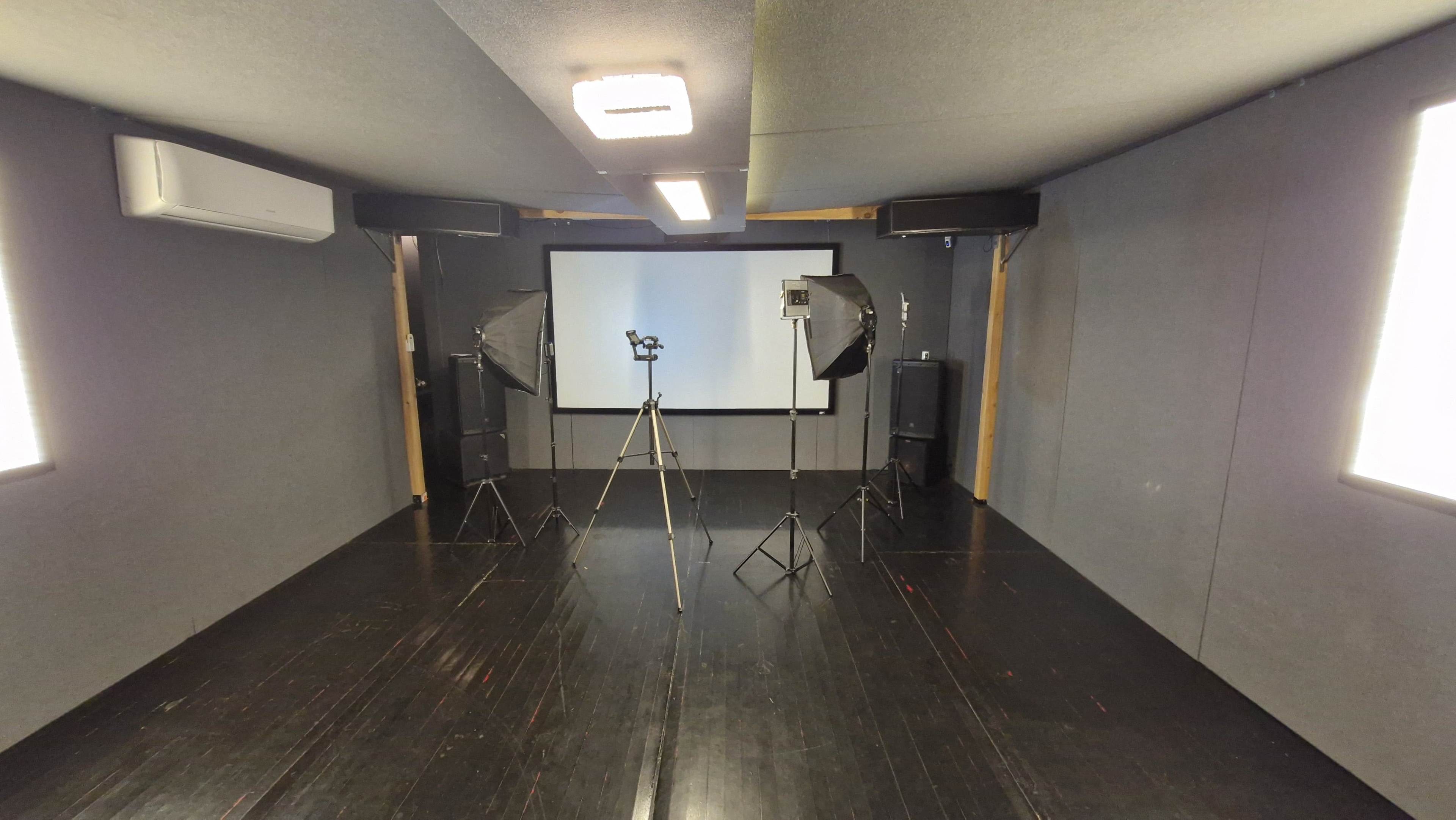 The image shows a photography studio setup with a backdrop, tripods, and lighting equipment positioned around a blank screen.