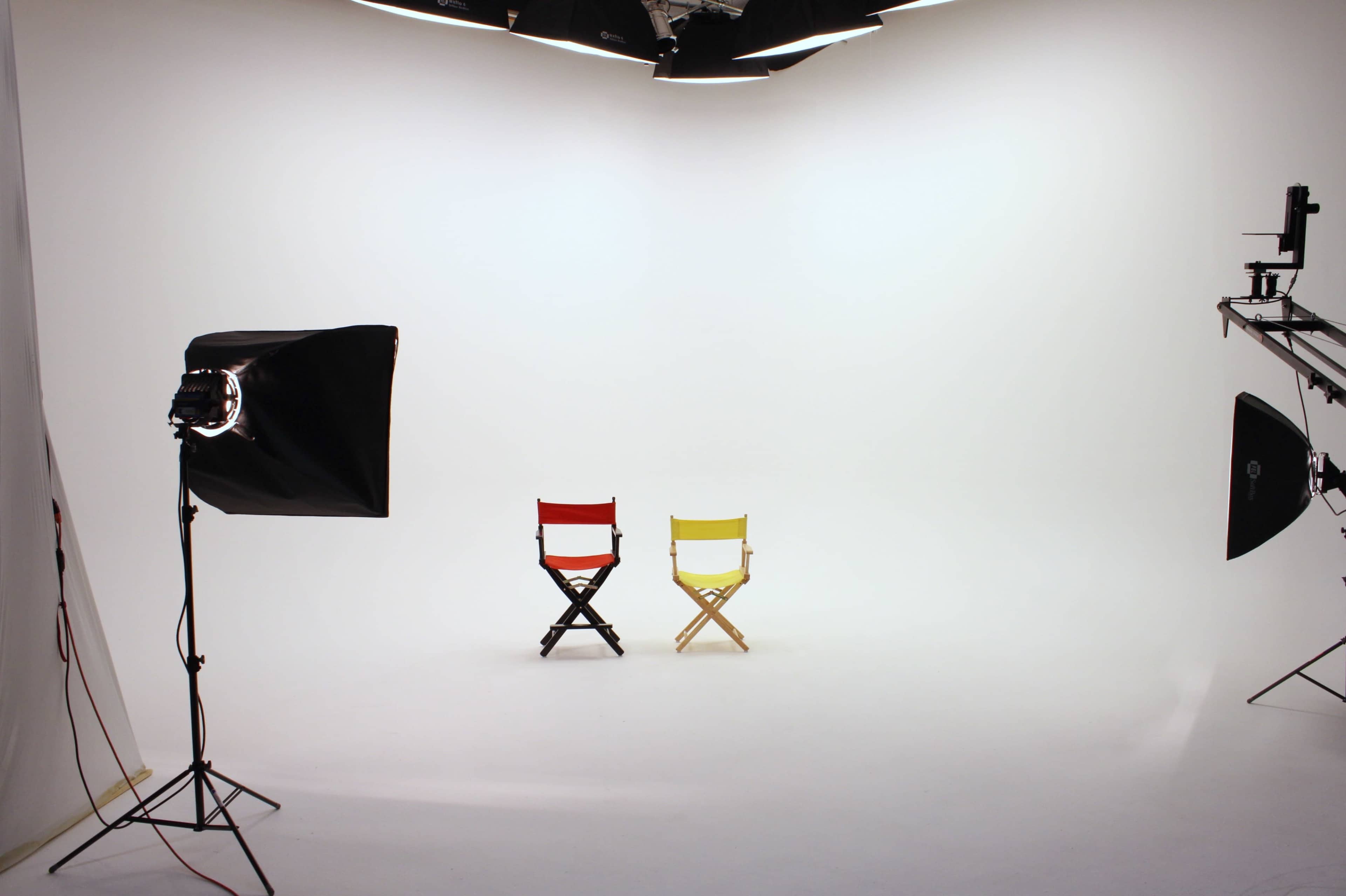 A minimalist photography studio featuring two director's chairs, one red and one yellow, under soft lighting.