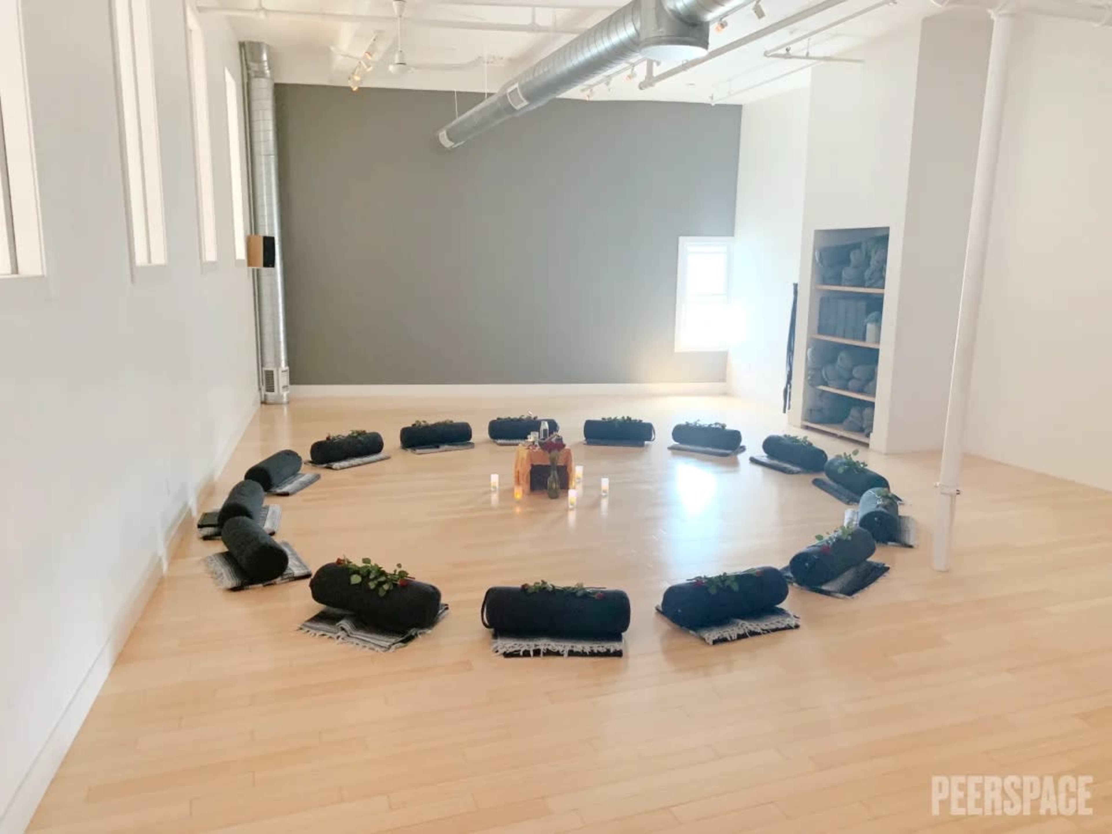 A circular arrangement of black meditation cushions is set up on a wooden floor in a bright, spacious room.