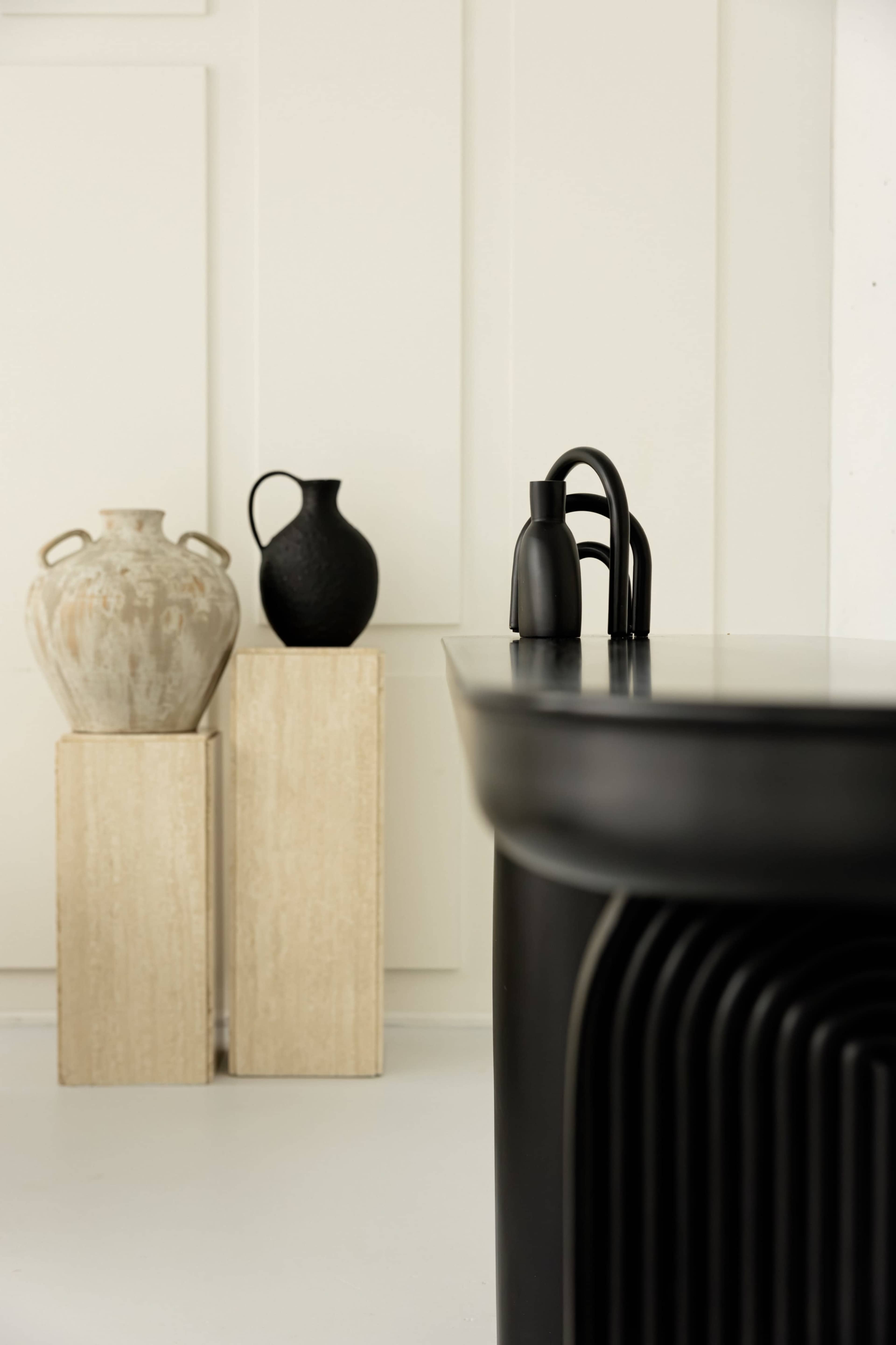 The image features a sleek black table with curved edges, accompanied by two decorative vases placed on pedestals in the background.