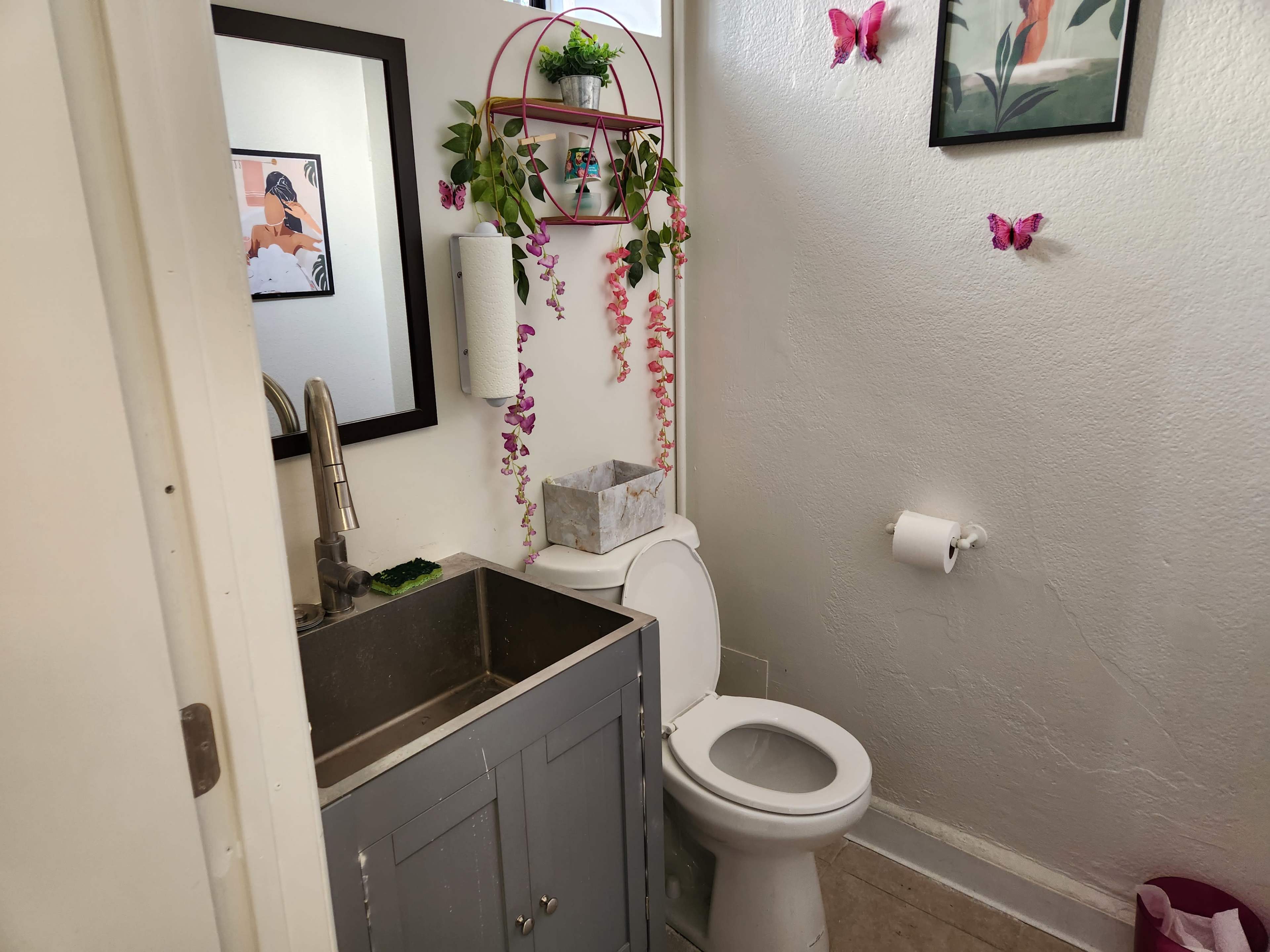 A small bathroom features a sink with a cabinet below, a toilet, and decorative elements including plants and butterflies on the walls.