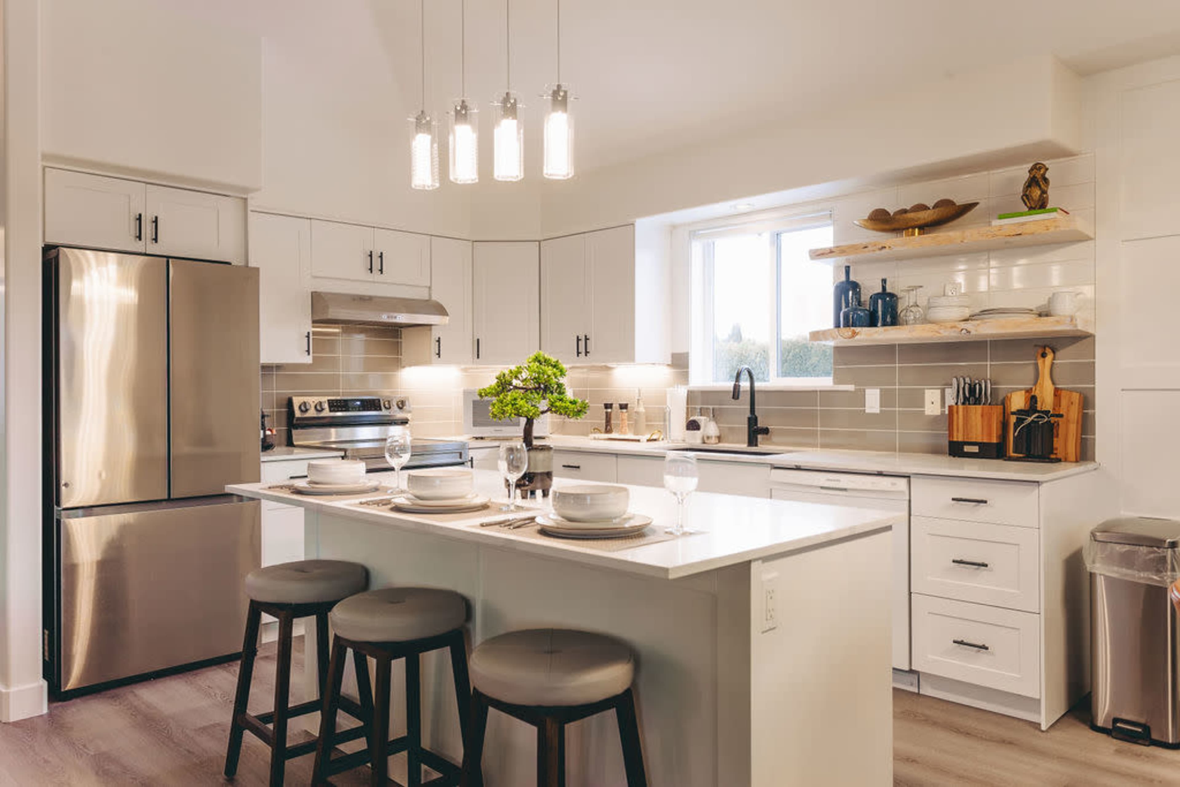 A modern kitchen features stainless steel appliances, a central island with seating, and a large window above the sink.