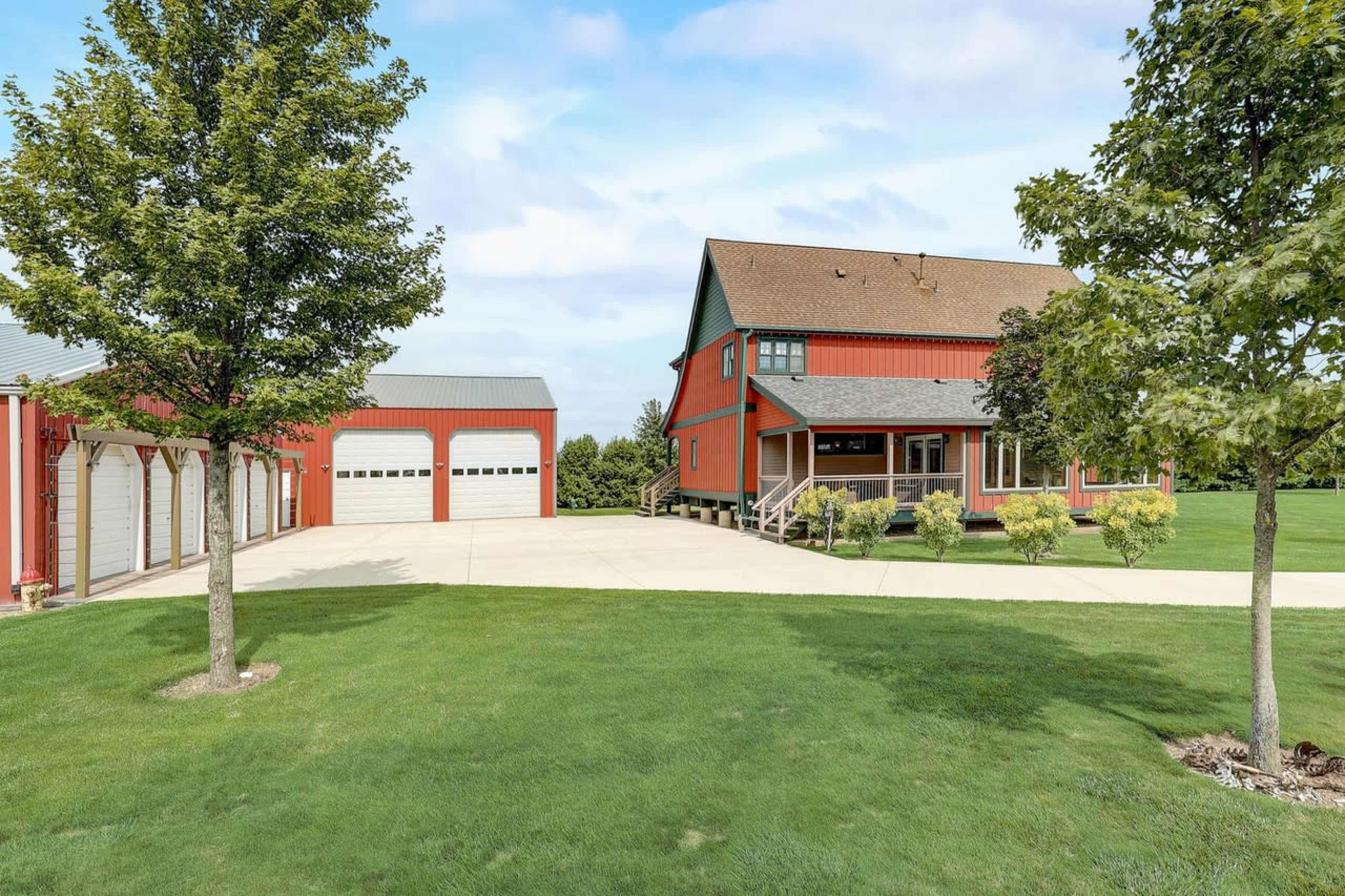 A red barn-style house stands alongside a matching red garage, set on a green lawn under a blue sky.