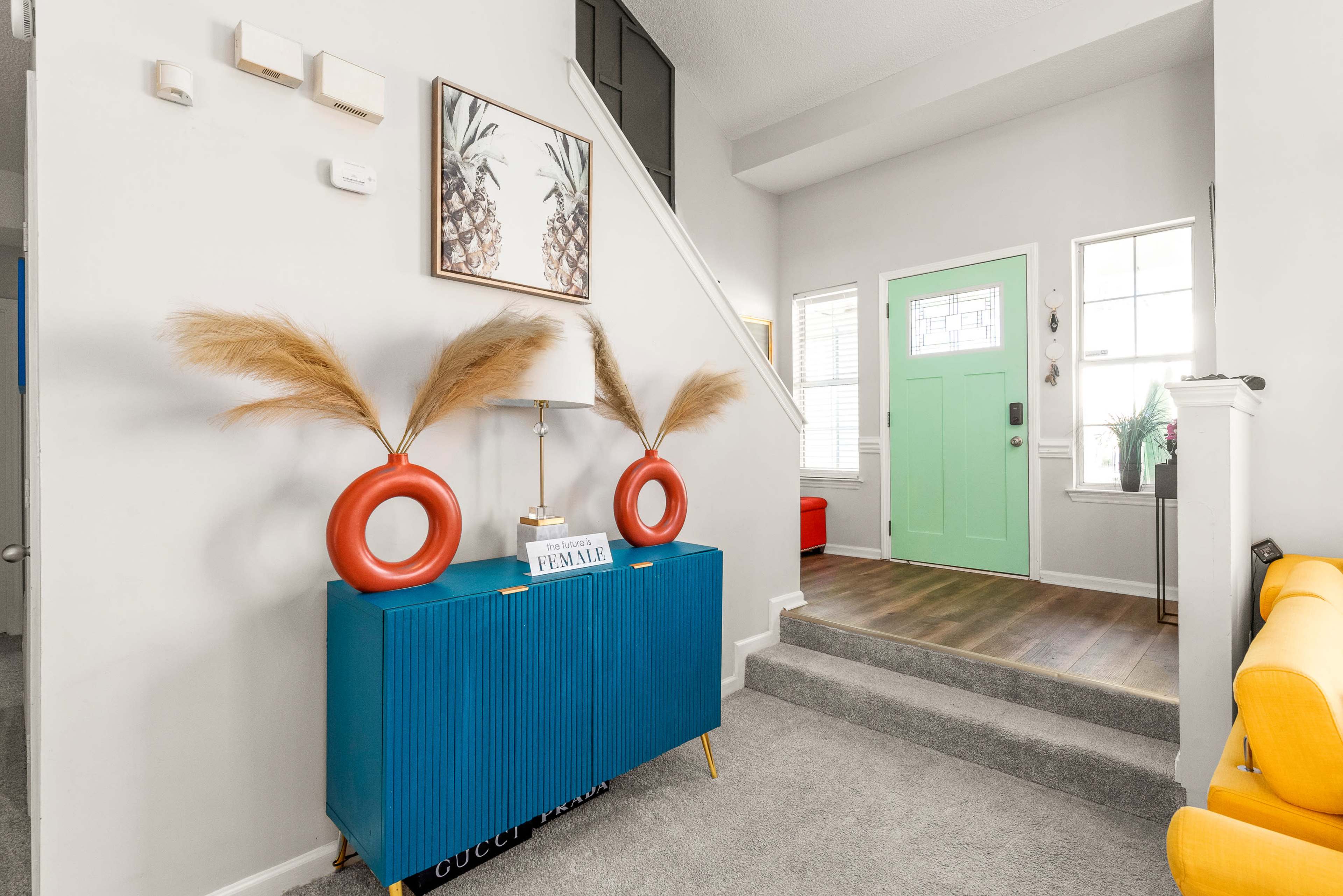 A vibrant entryway features a teal console table adorned with decorative items and large plants, leading up to a staircase and a door painted in a bright green.