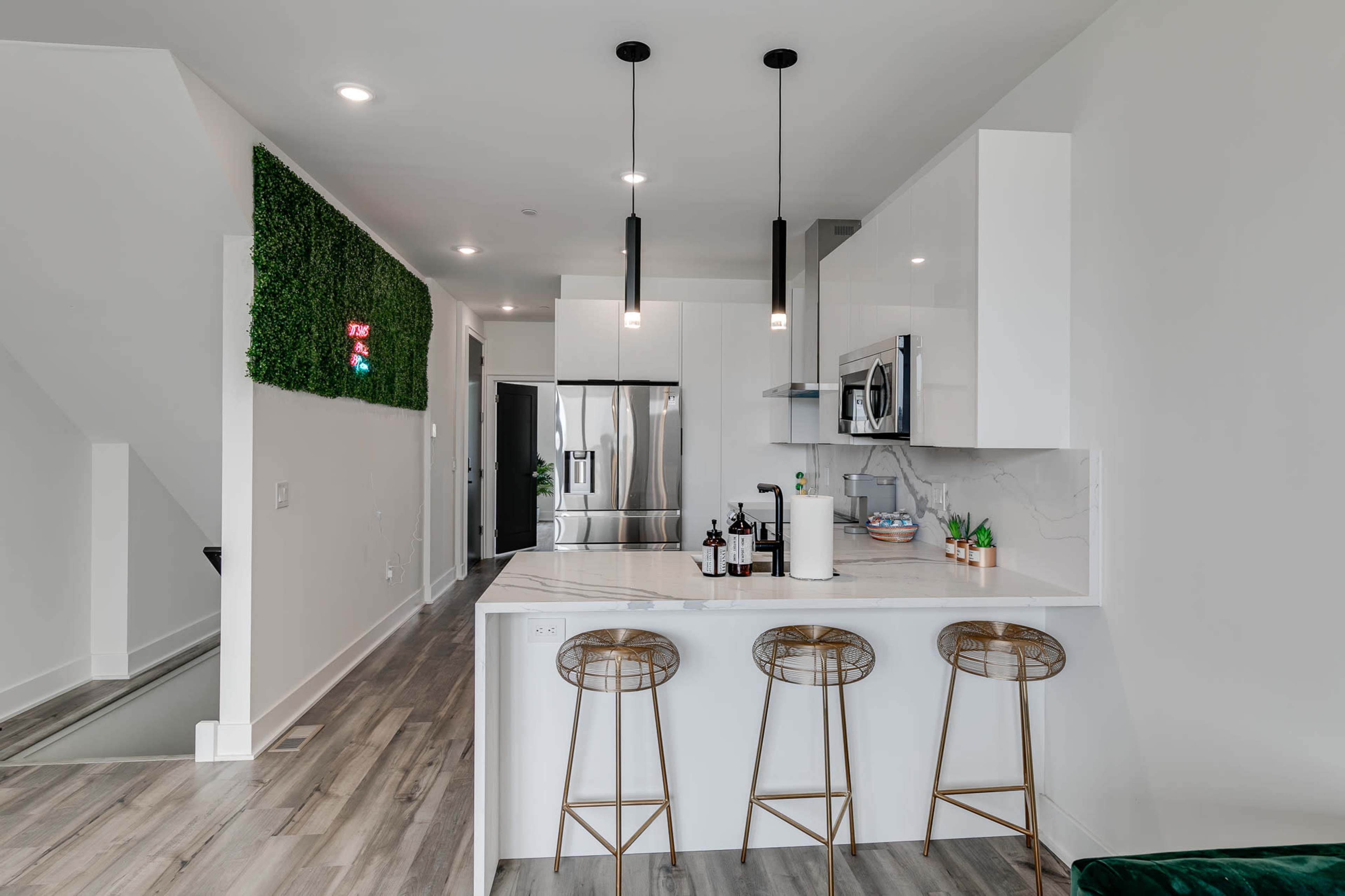 A modern kitchen with a white countertop, three bar stools, stainless steel appliances, and green wall decor.