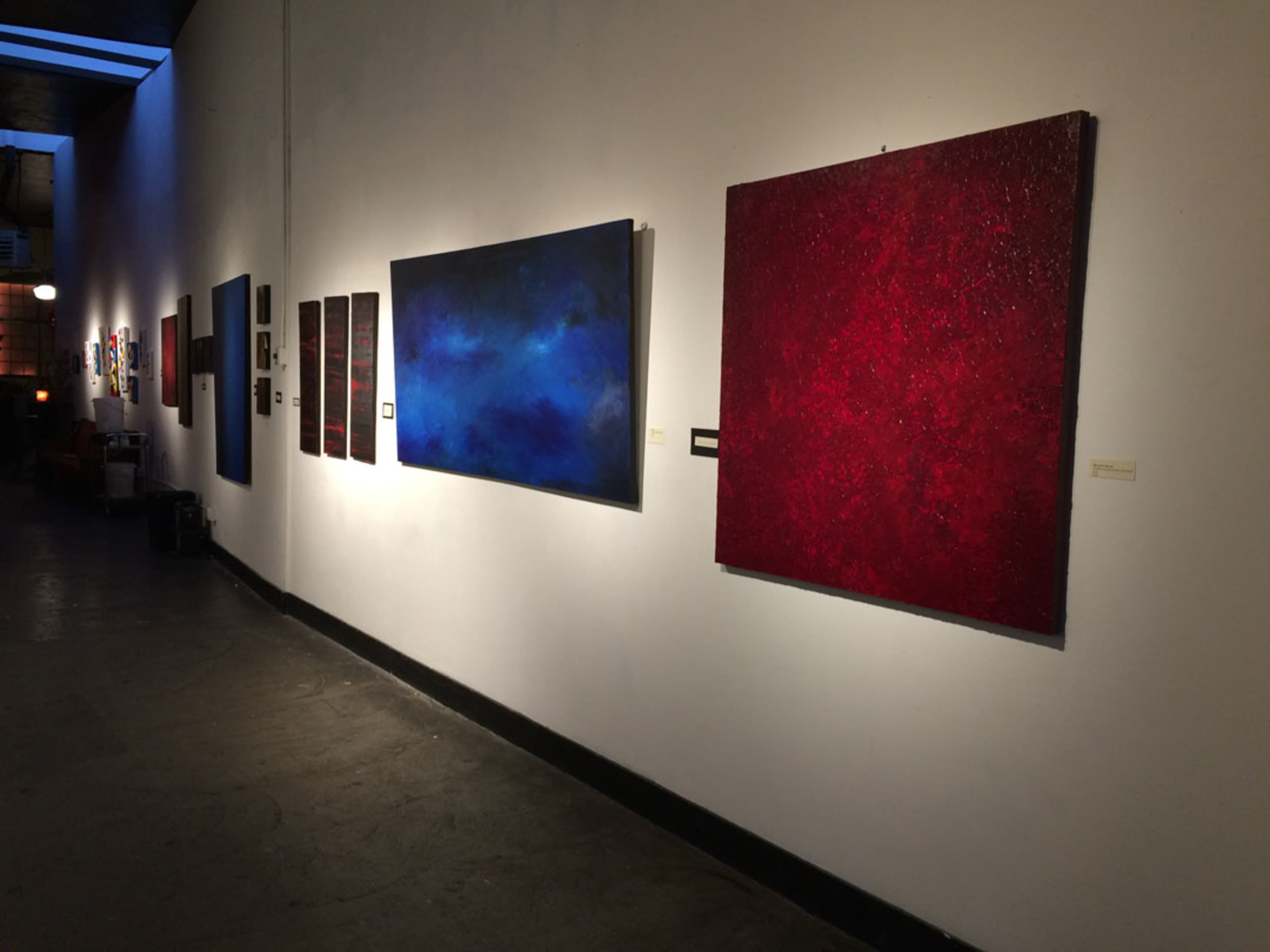 A gallery wall displaying various abstract paintings in blue and red tones.