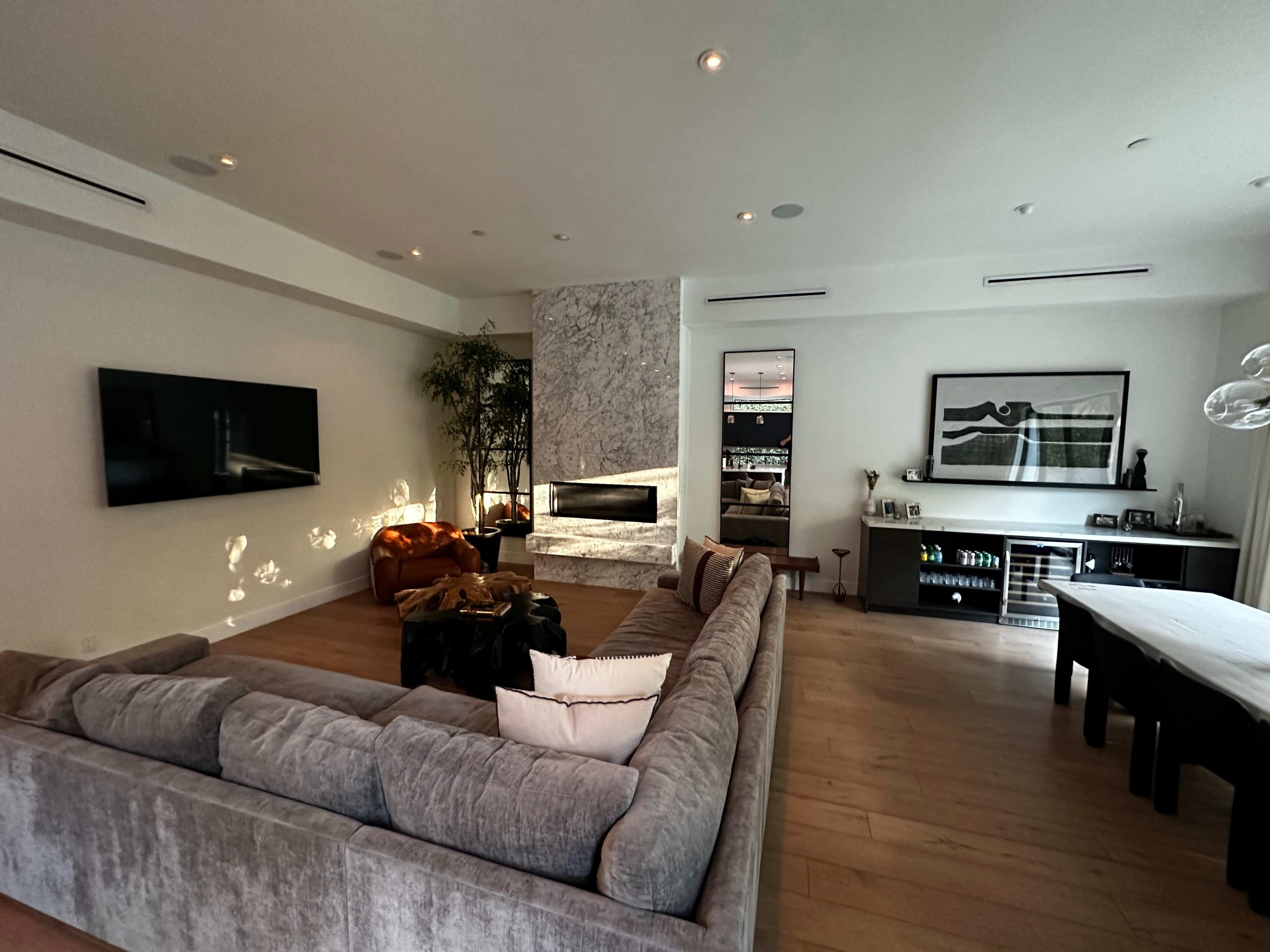 A modern living room featuring a large gray sectional sofa, a marble fireplace, a wall-mounted TV, and a dark wood sideboard.