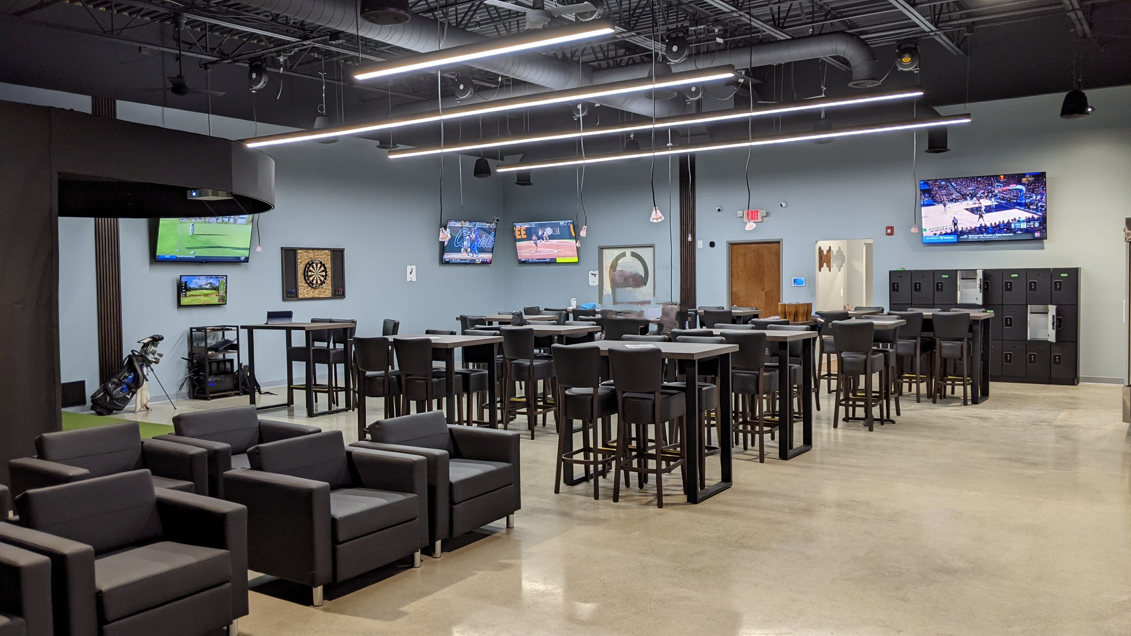 A spacious recreational room featuring several black high-top tables, leather chairs, and multiple flat-screen TVs mounted on the walls.