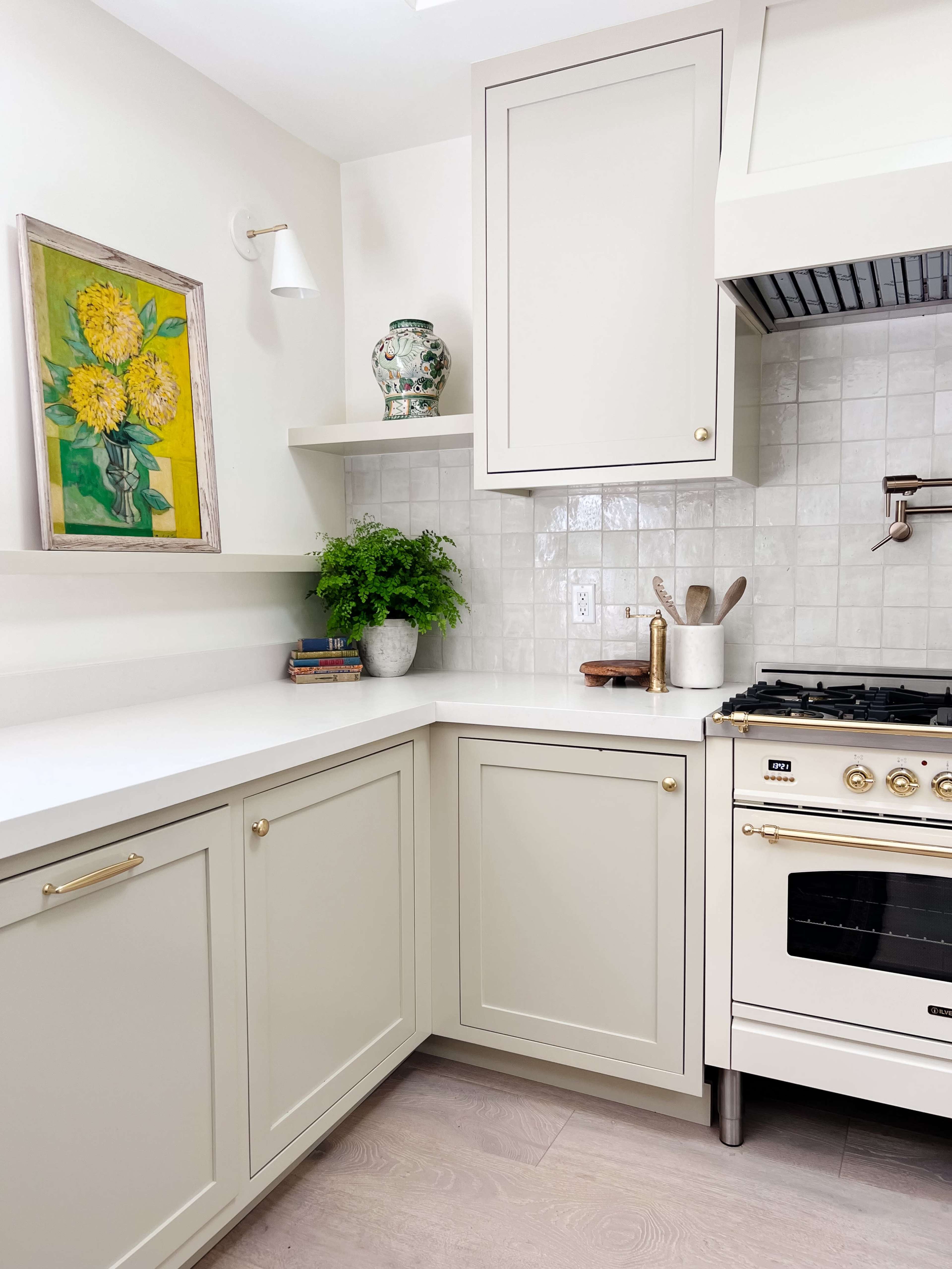 A modern kitchen with light gray cabinetry, a white countertop, a stovetop, and decorative items on shelves.