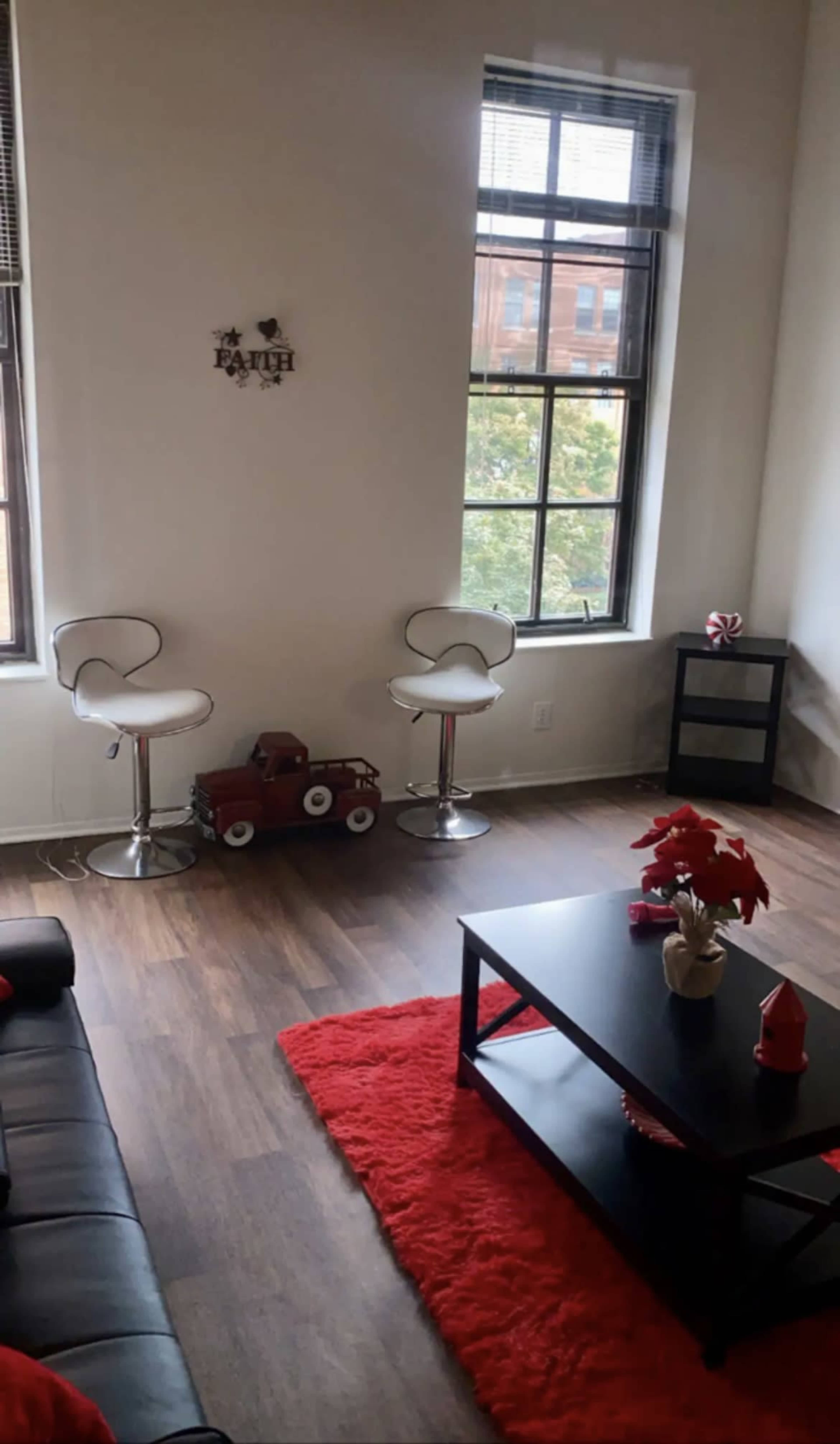 A modern living room featuring two high-backed chairs, a small red toy car, a black coffee table, and a decorative arrangement on a red rug.