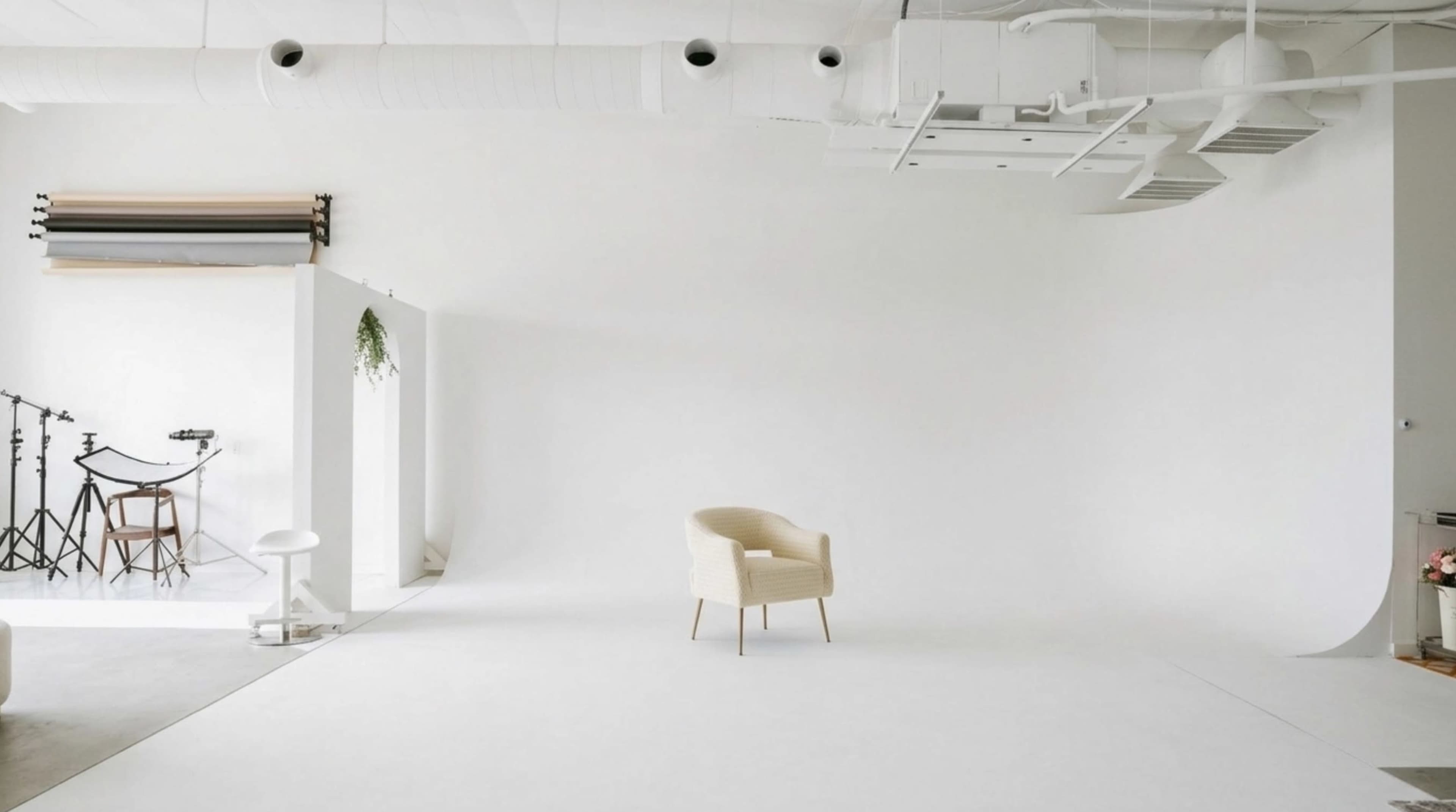 A minimalist studio space features a white backdrop, a single chair, and various photography equipment in the background.