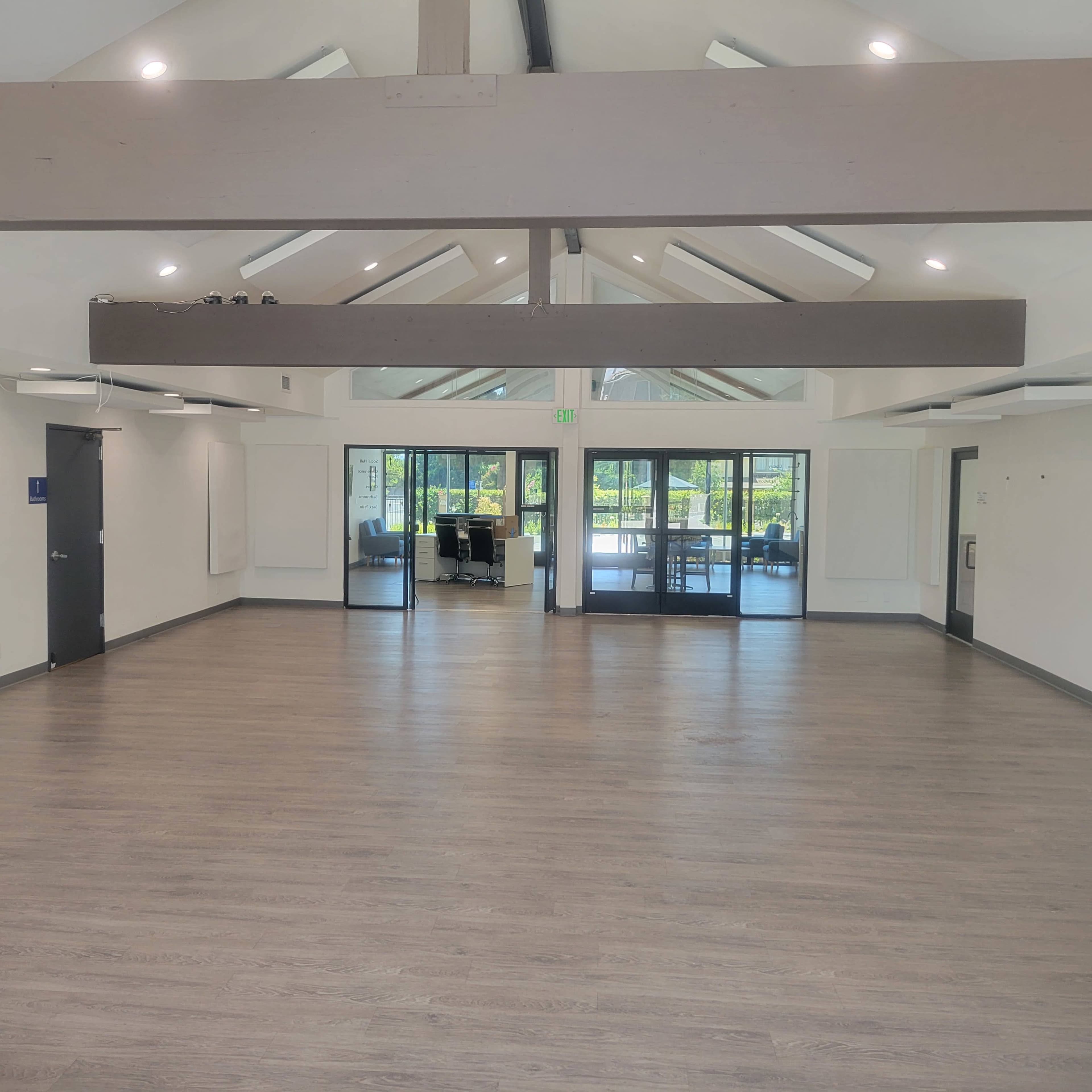 An empty room with wooden flooring, high ceilings, and large glass doors leading to an outdoor area.